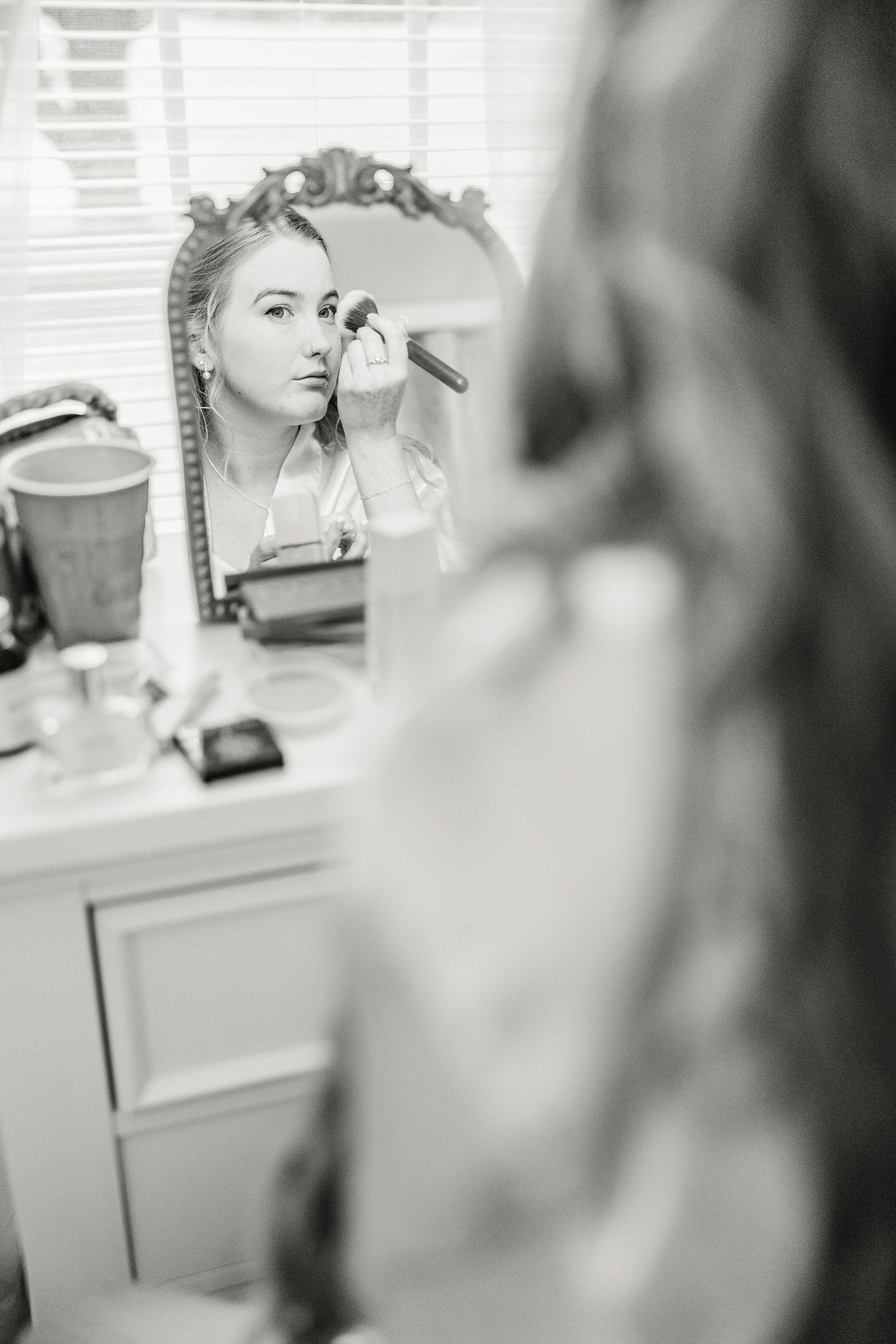 Black and white image of makeup reflected in a vanity mirror wedding groom bride wilmington North Carolina photographer light and airy