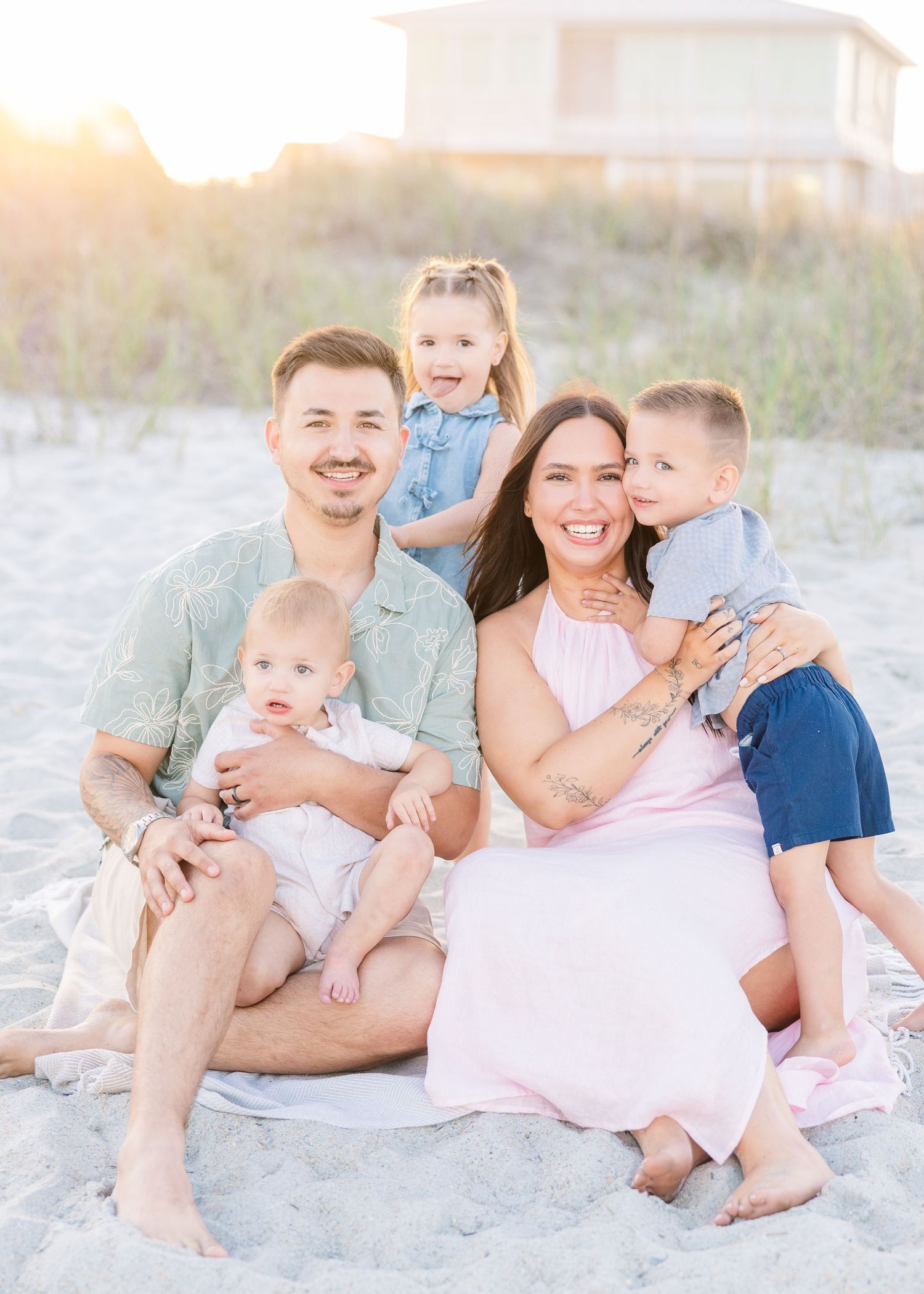 Joyful family beach portrait at sunset with parents and three young children on sandy shore.