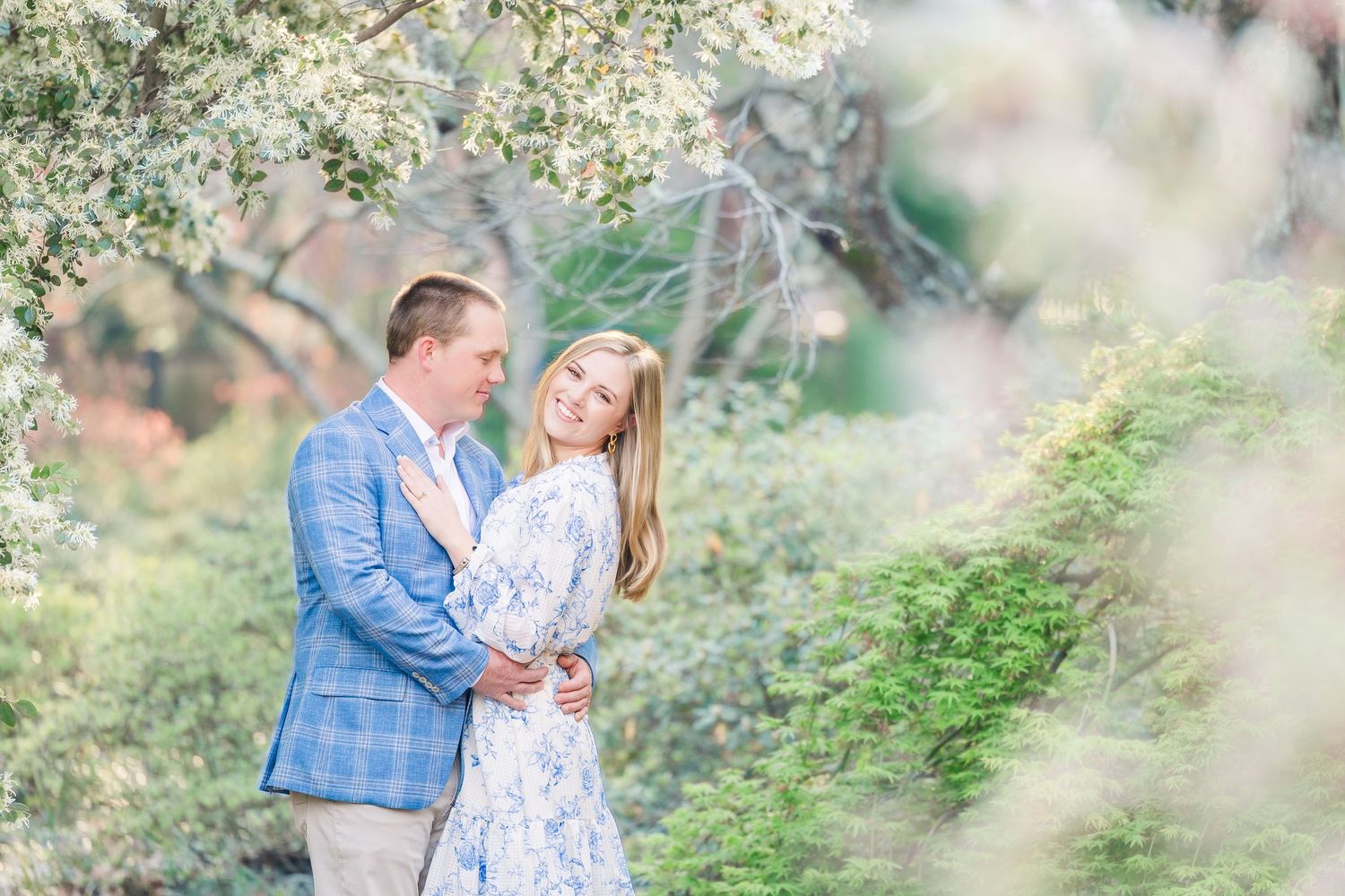 A couple in coordinating blue and white outfits share a romantic moment together in a lush garden setting.