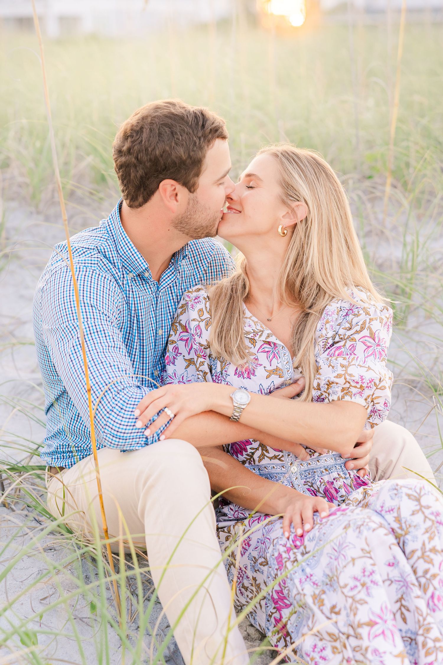 Romantic kiss shared on sandy beach during sunset with sea grass surrounding.