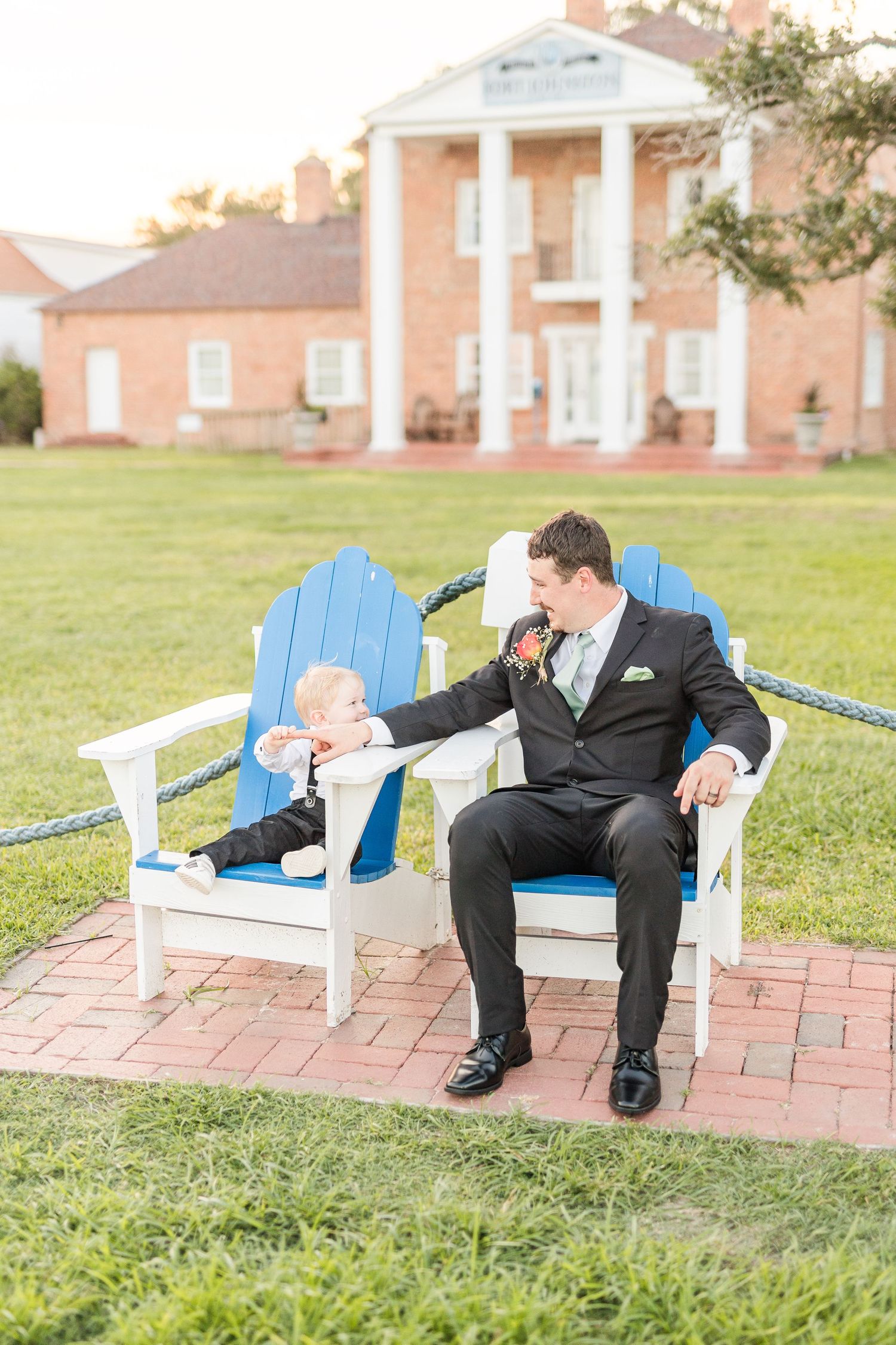 Wedding party relaxing in blue Adirondack chairs on brick patio near colonial style building southport elopement wedding bride groom light