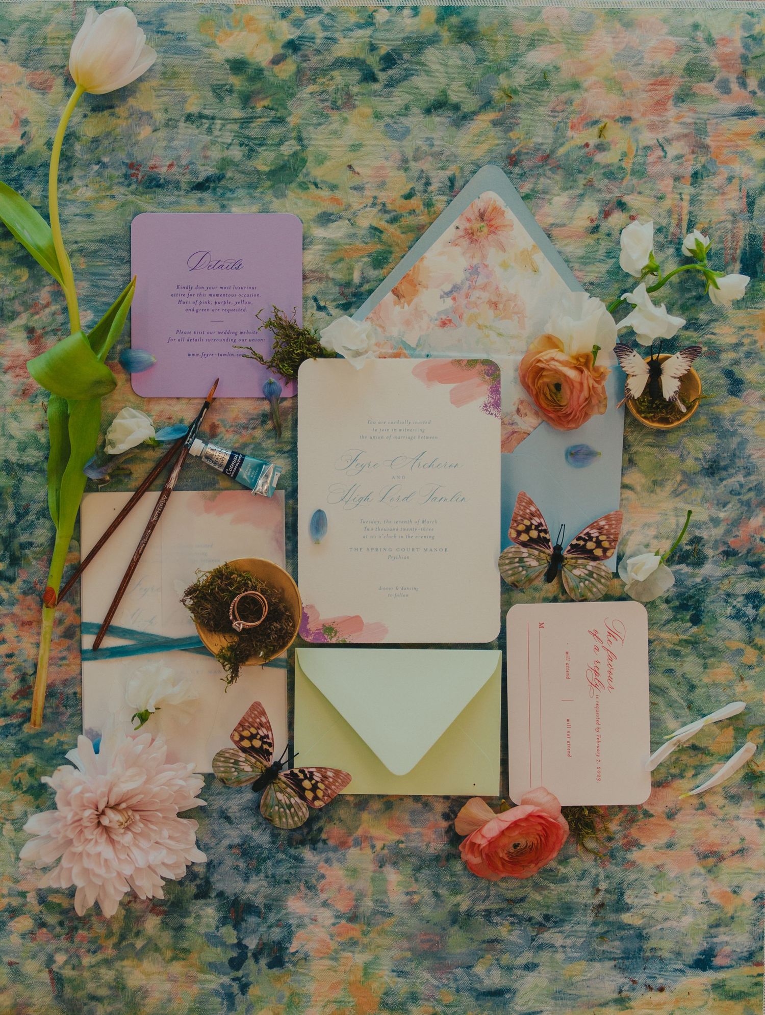 Pastel floral wedding invitation flat lay with rings and paintbrushes, styled by a Wichita wedding photographer.