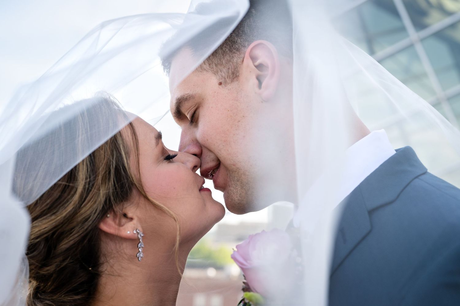 Bride and groom sharing a moment photographed through a flowing white veil.