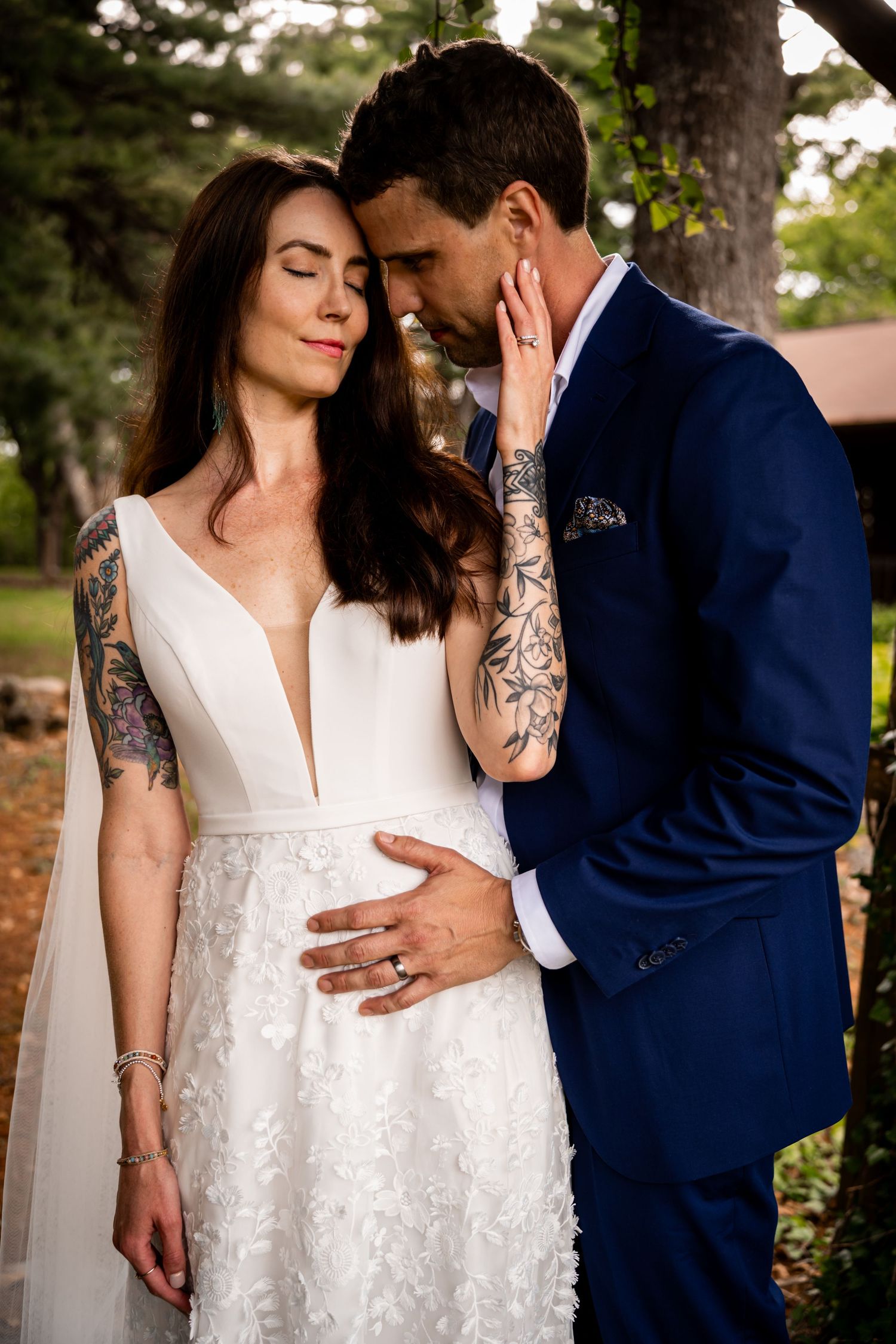 Bride in a white dress with visible tattoos standing close with her partner in a navy suit.
