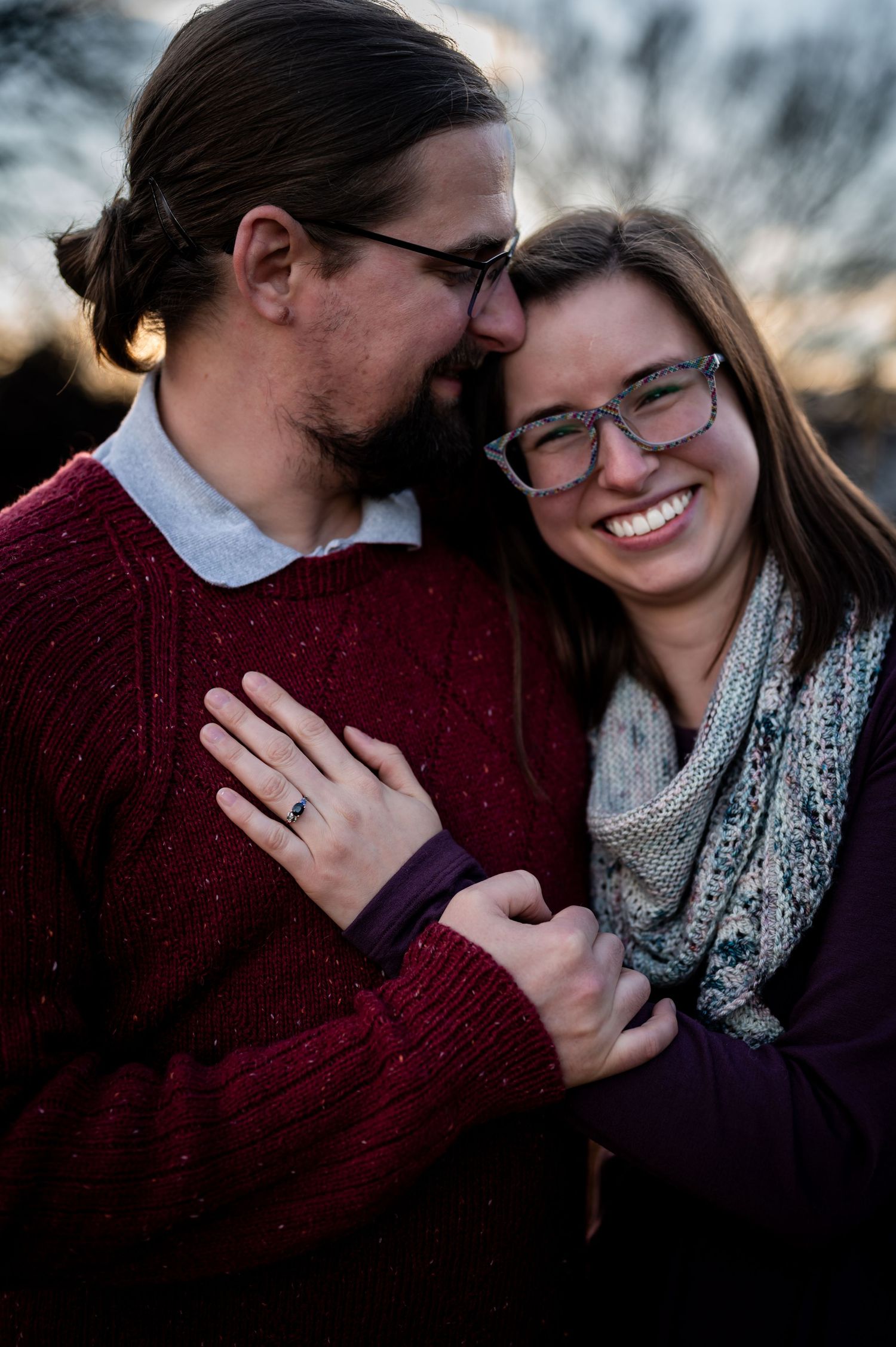 Engaged couple standing together outdoors in winter, wearing warm sweaters.
