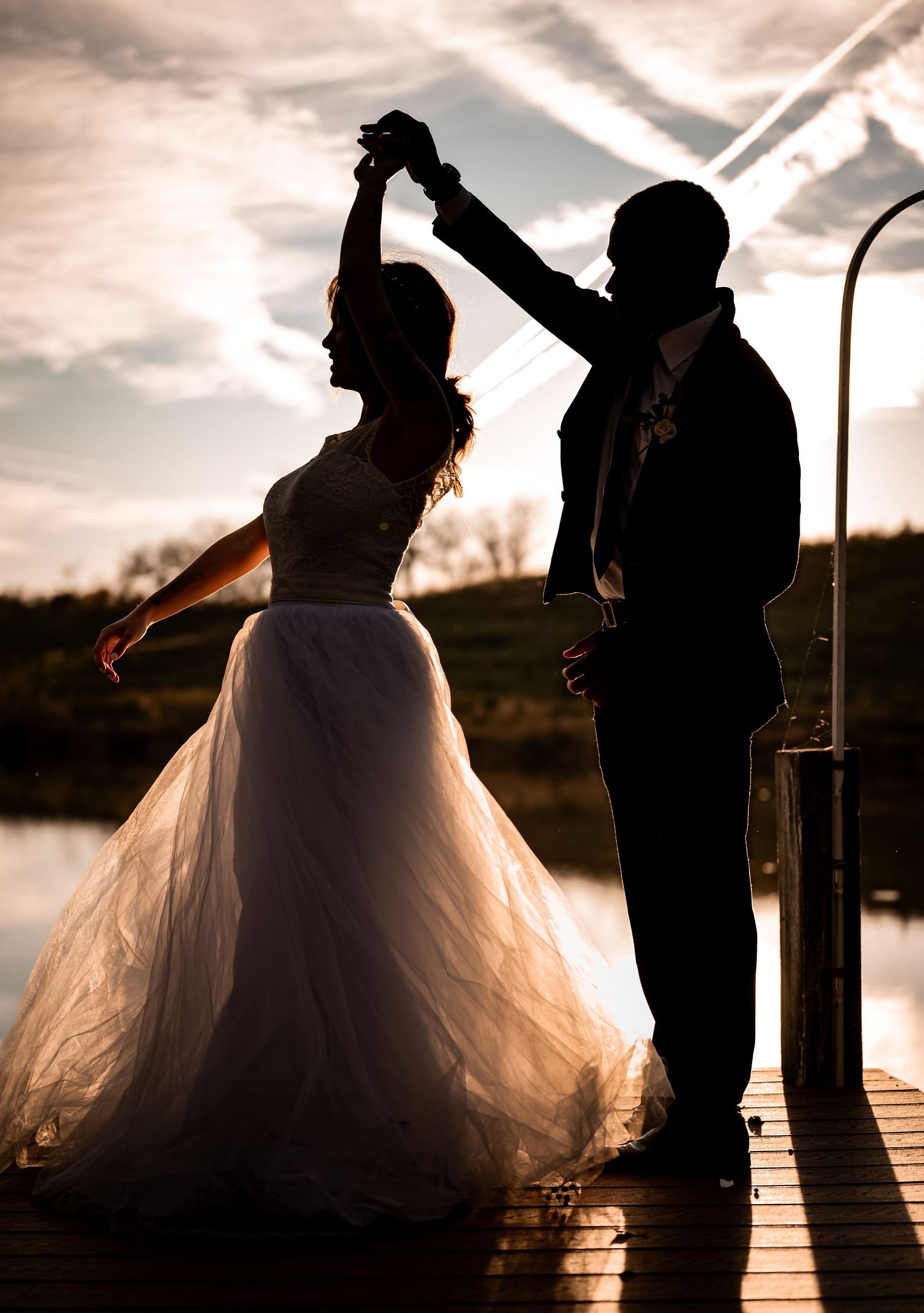 Silhouette of a bride and groom standing together on a dock at sunset.