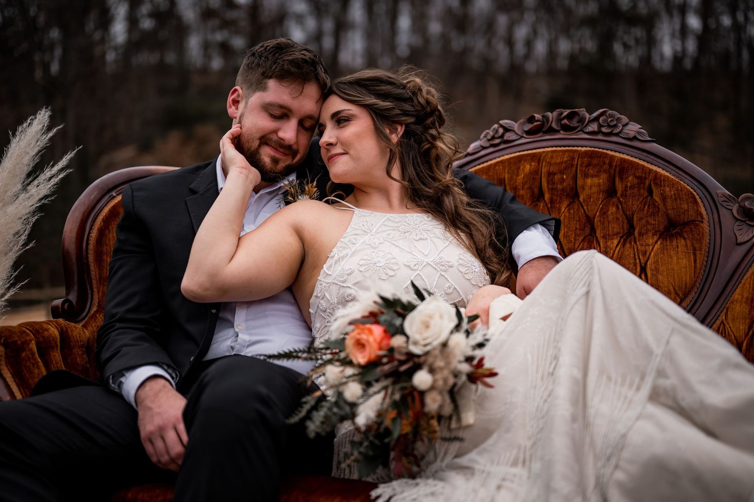 Bride and groom seated together on vintage furniture during a softly lit wedding portrait.