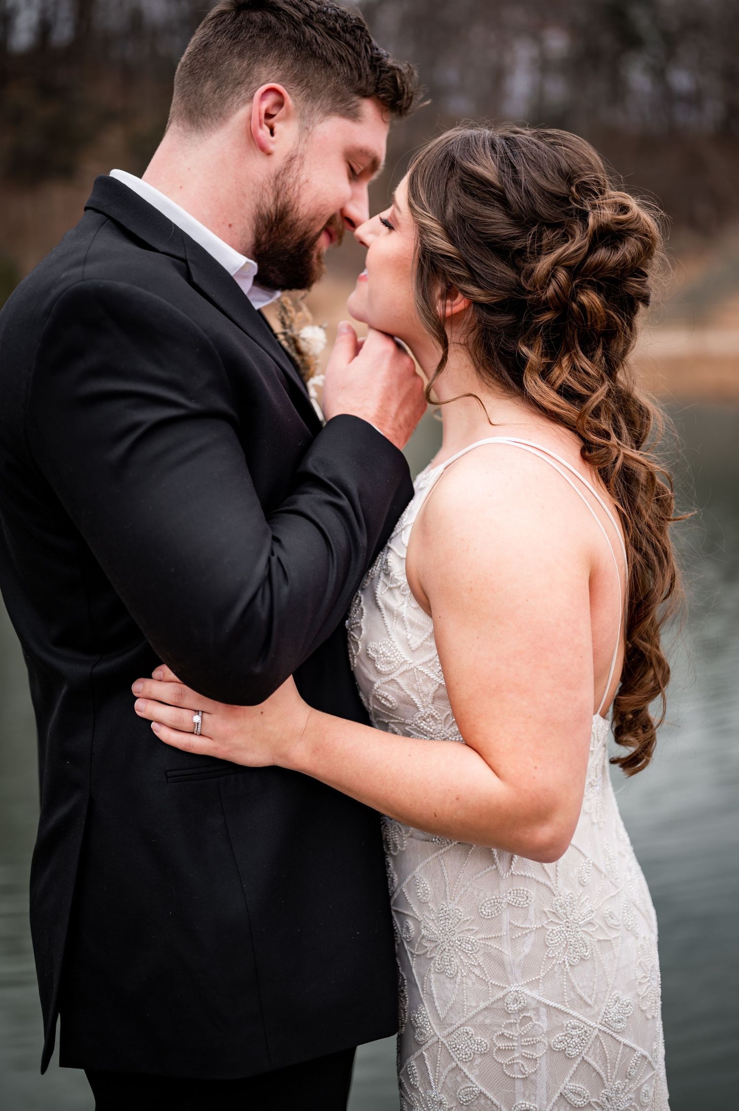 Bride and groom standing close together beside a lake during a winter wedding.