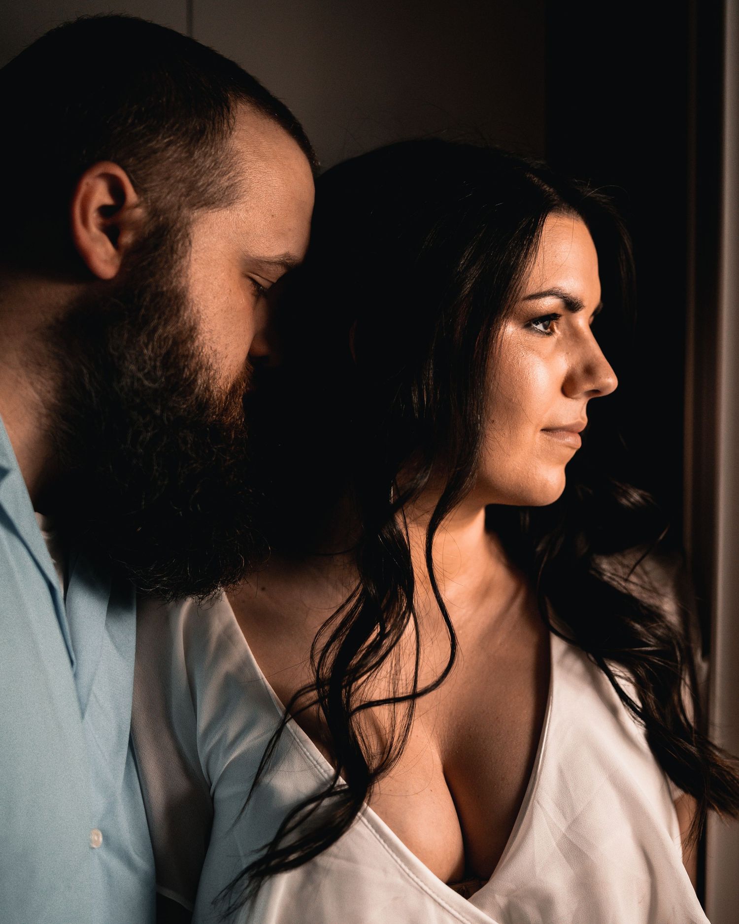 Side-lit portrait of a couple standing close together in low light.