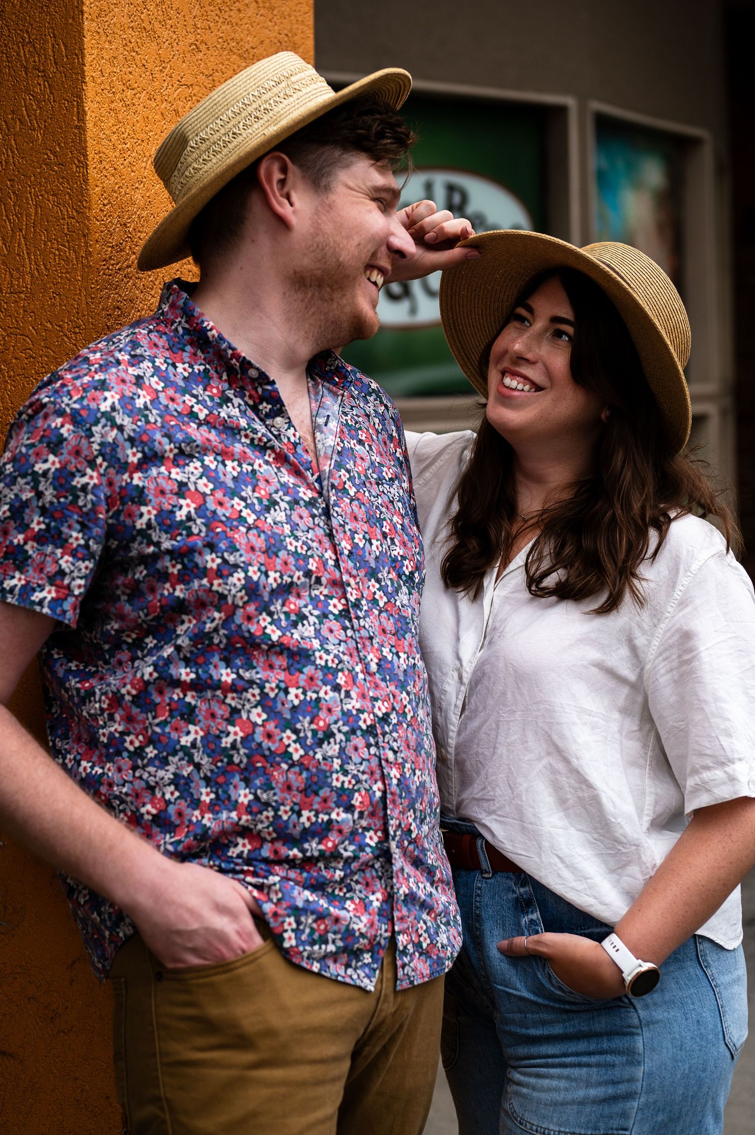 Couple standing together against a warm-toned wall wearing floral and white outfits.