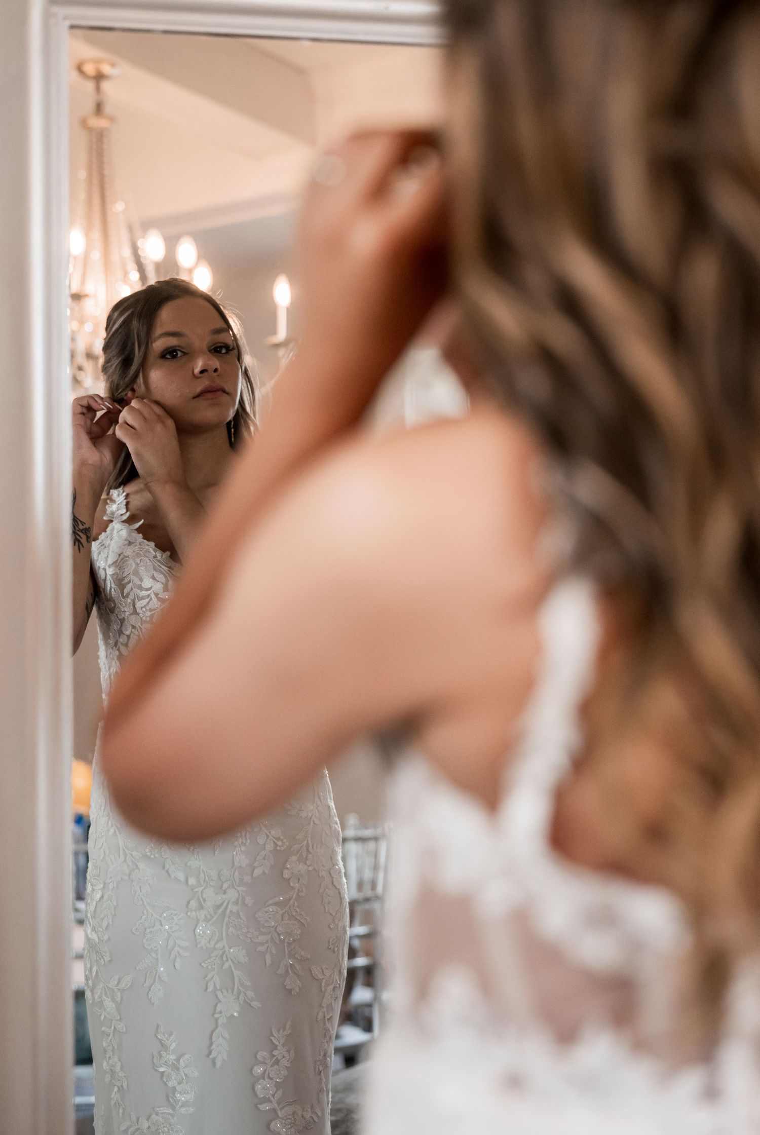 Bride wearing a lace wedding dress looking at her reflection in a mirror.
