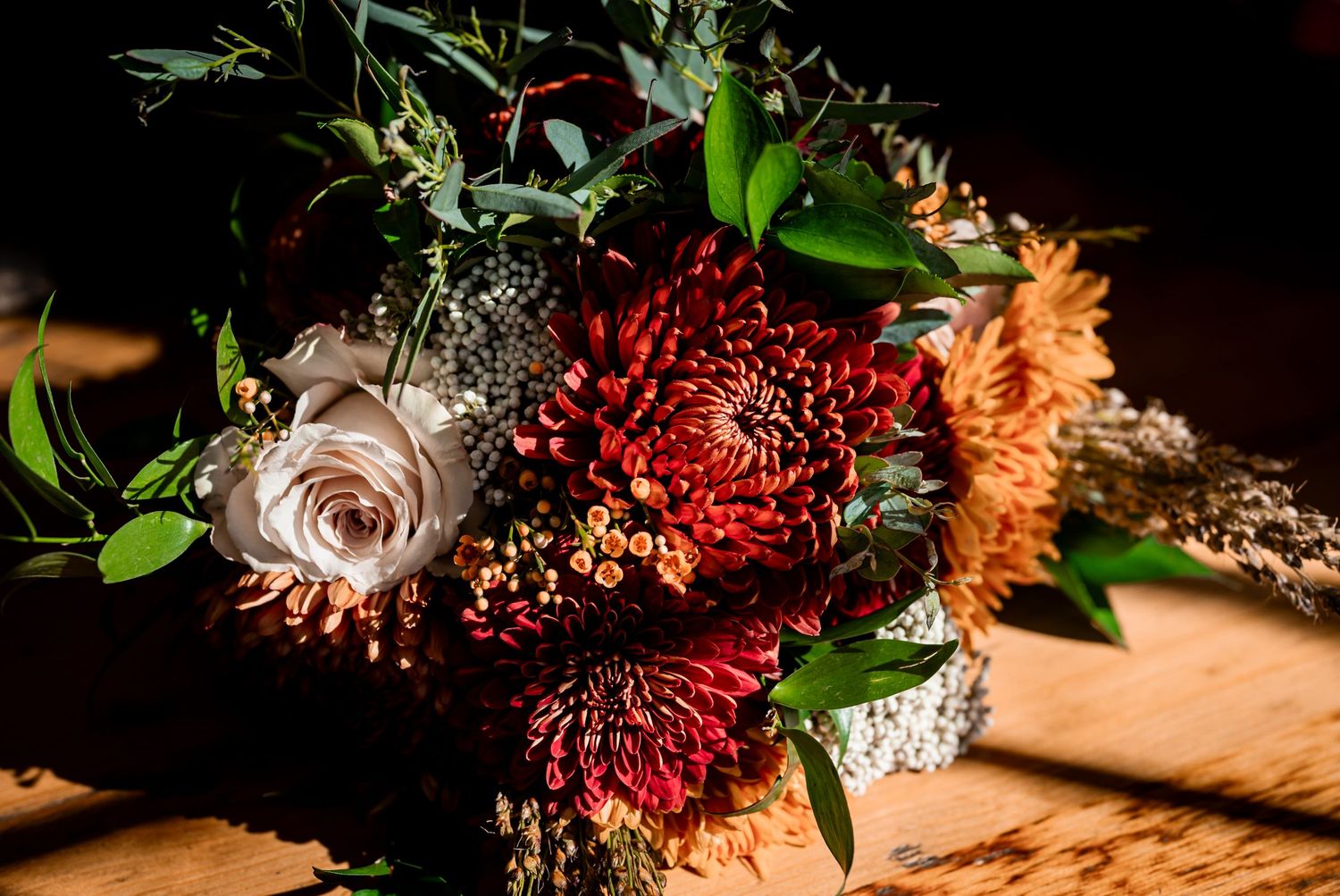 Wedding floral arrangement featuring deep red and orange blooms on a dark background.