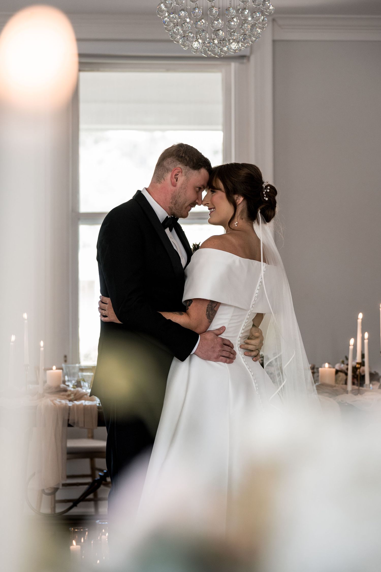 Bride and groom standing together in a candlelit room with a crystal chandelier.
