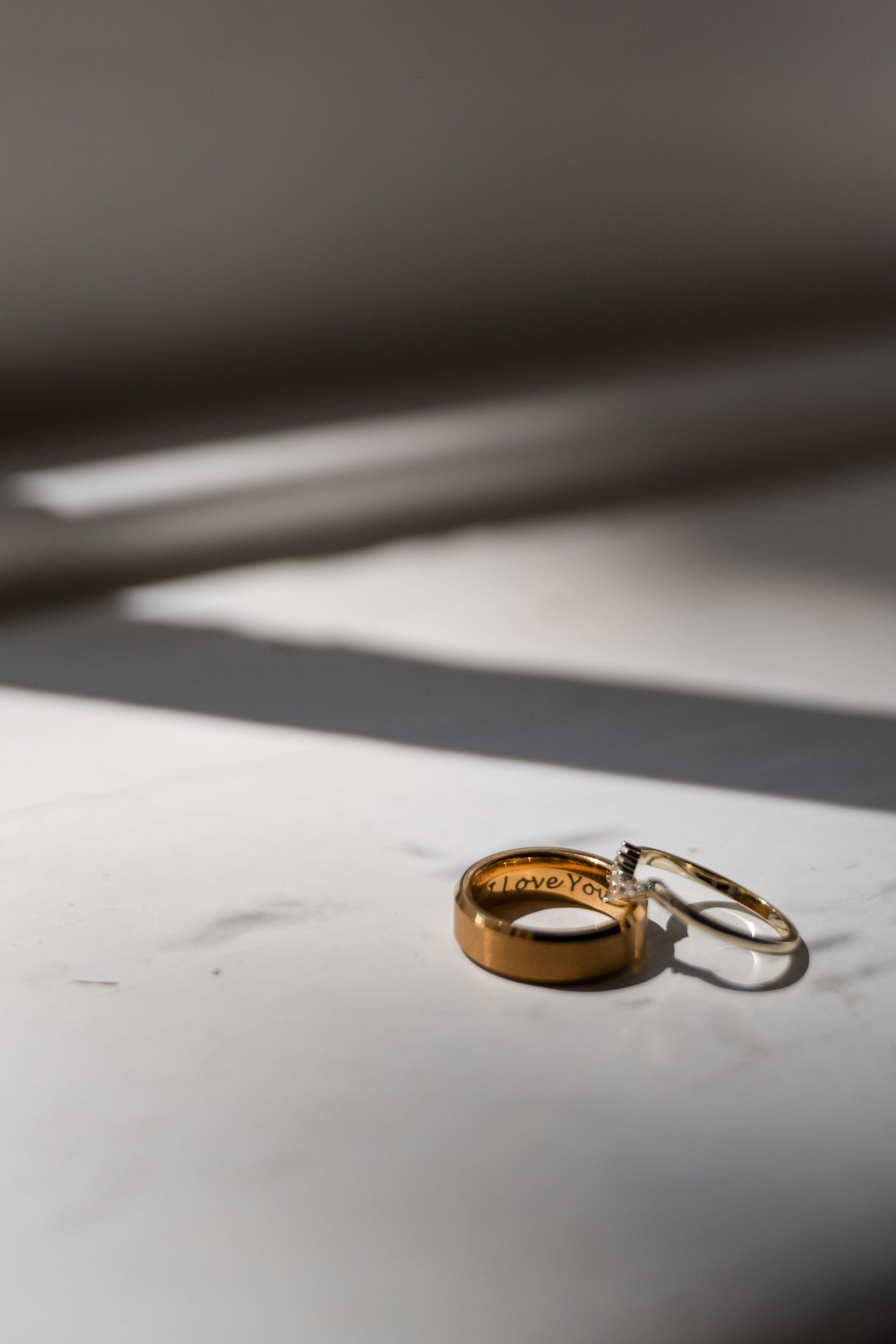 Wedding rings casting shadows on a white surface in natural light.