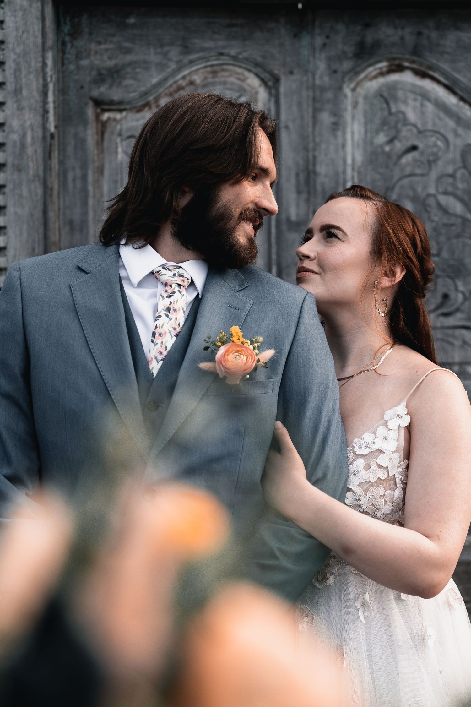 Bride and groom standing together against a textured stone wall backdrop.