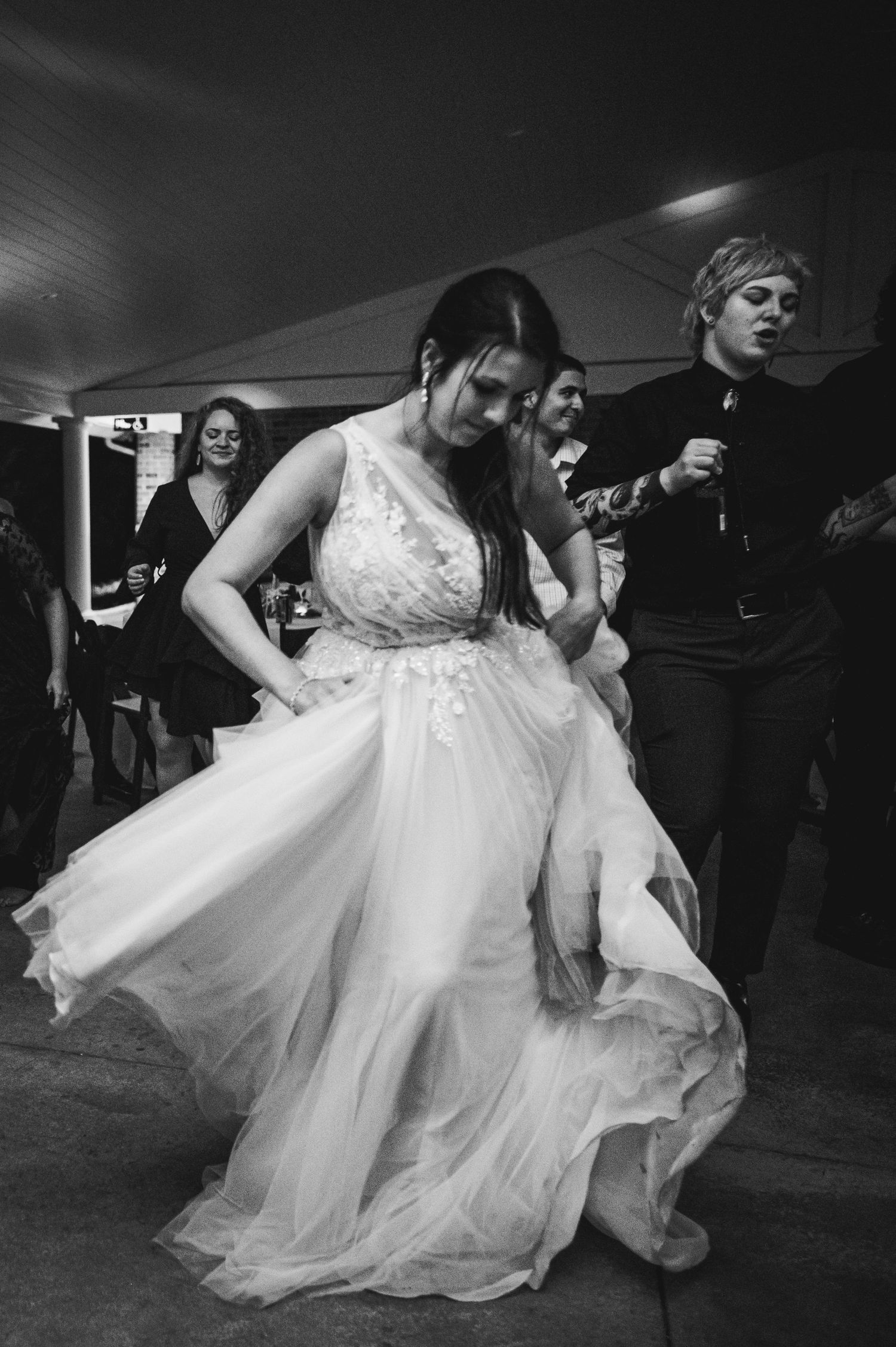 Black and white photo of bride dancing in flowing dress at a wedding reception.