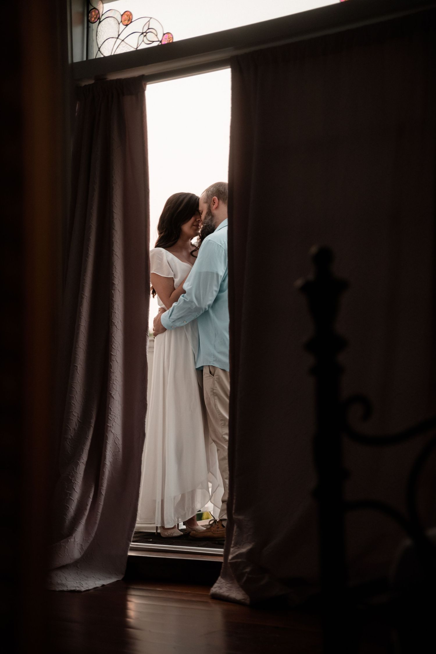 Silhouette of a couple standing by a window framed by dark curtains.