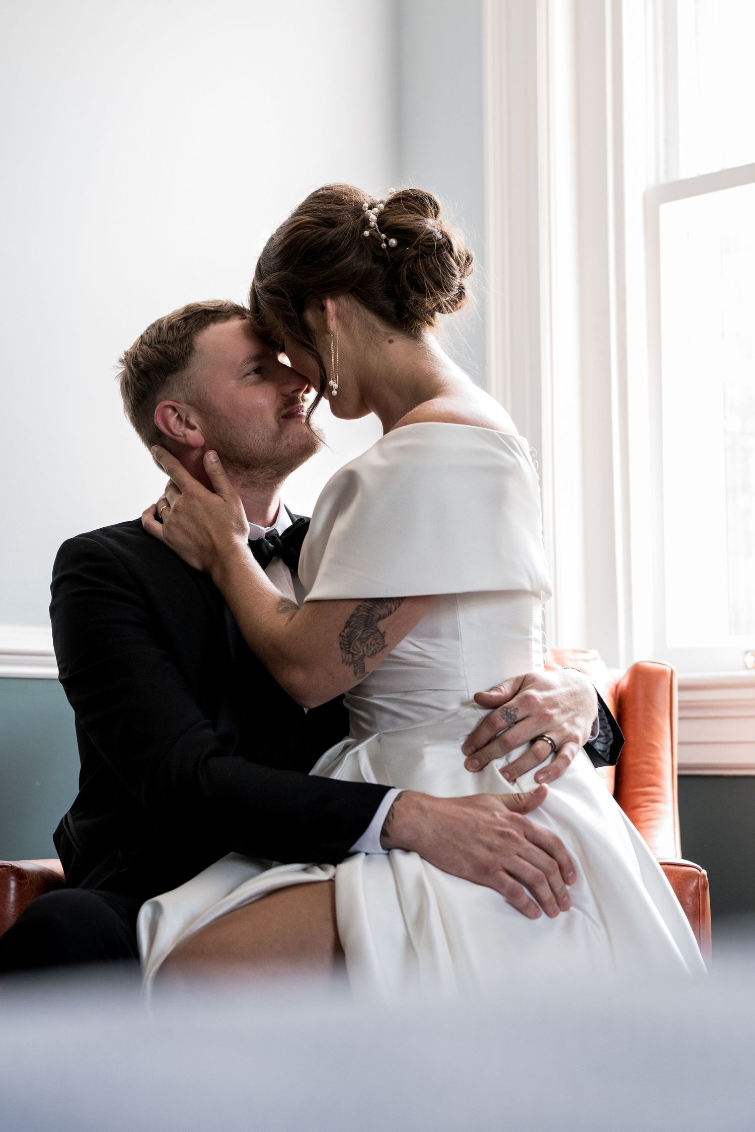 Couple sitting together on a white couch near a bright window.