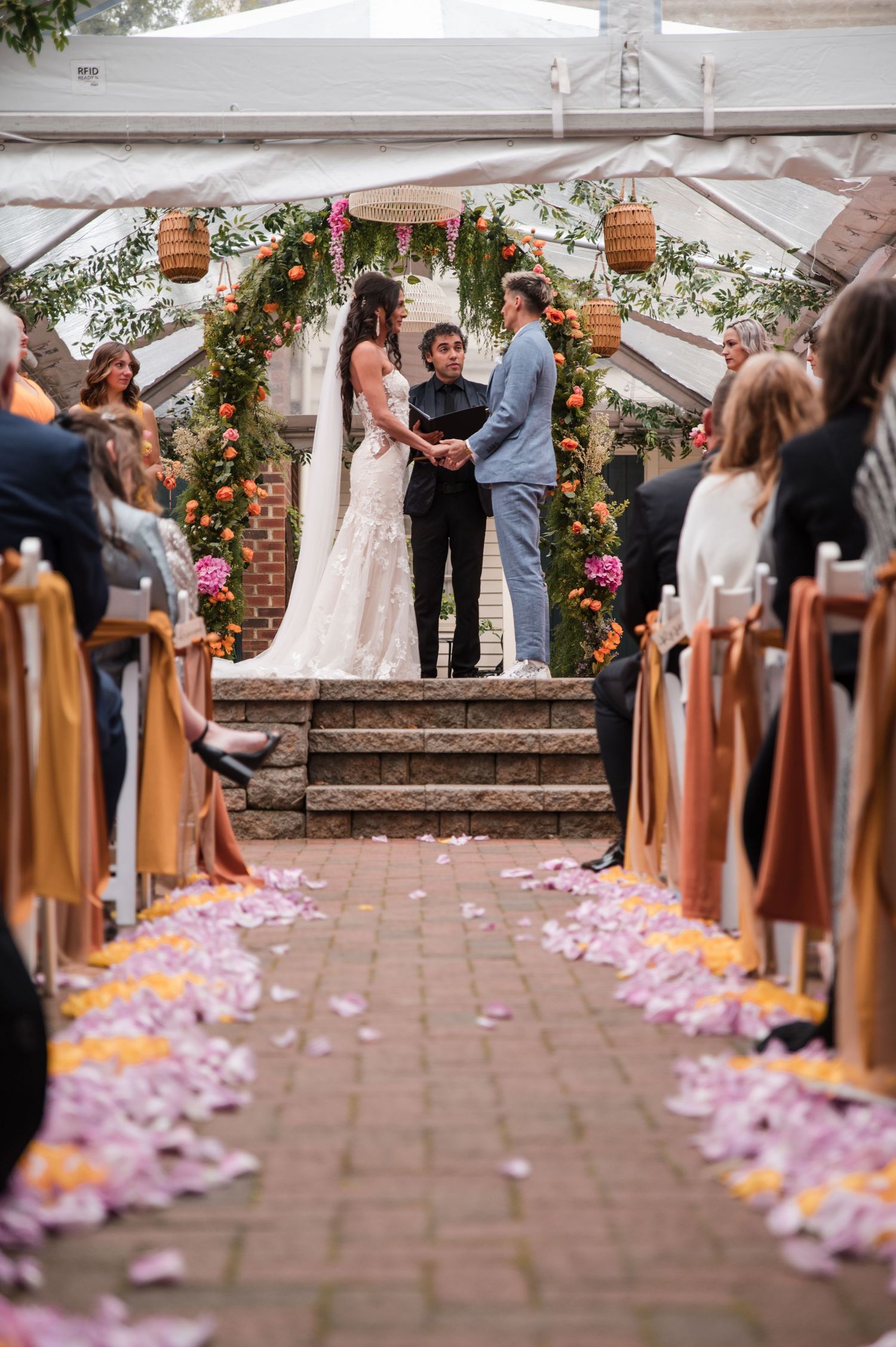 Wedding ceremony aisle lined with pink rose petals beneath a white tent canopy.