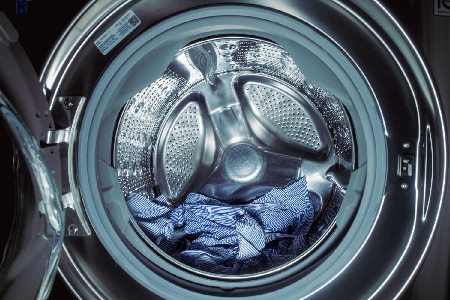 Front-loading washing machine drum spinning with blue laundry inside.