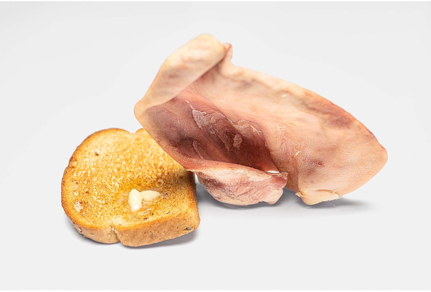 Thinly sliced prosciutto ham served alongside a golden toasted bread slice on a white background.