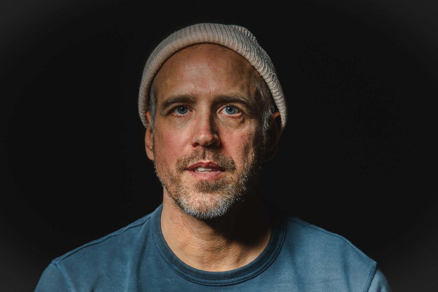 Portrait of person wearing blue shirt and beanie against dark background.