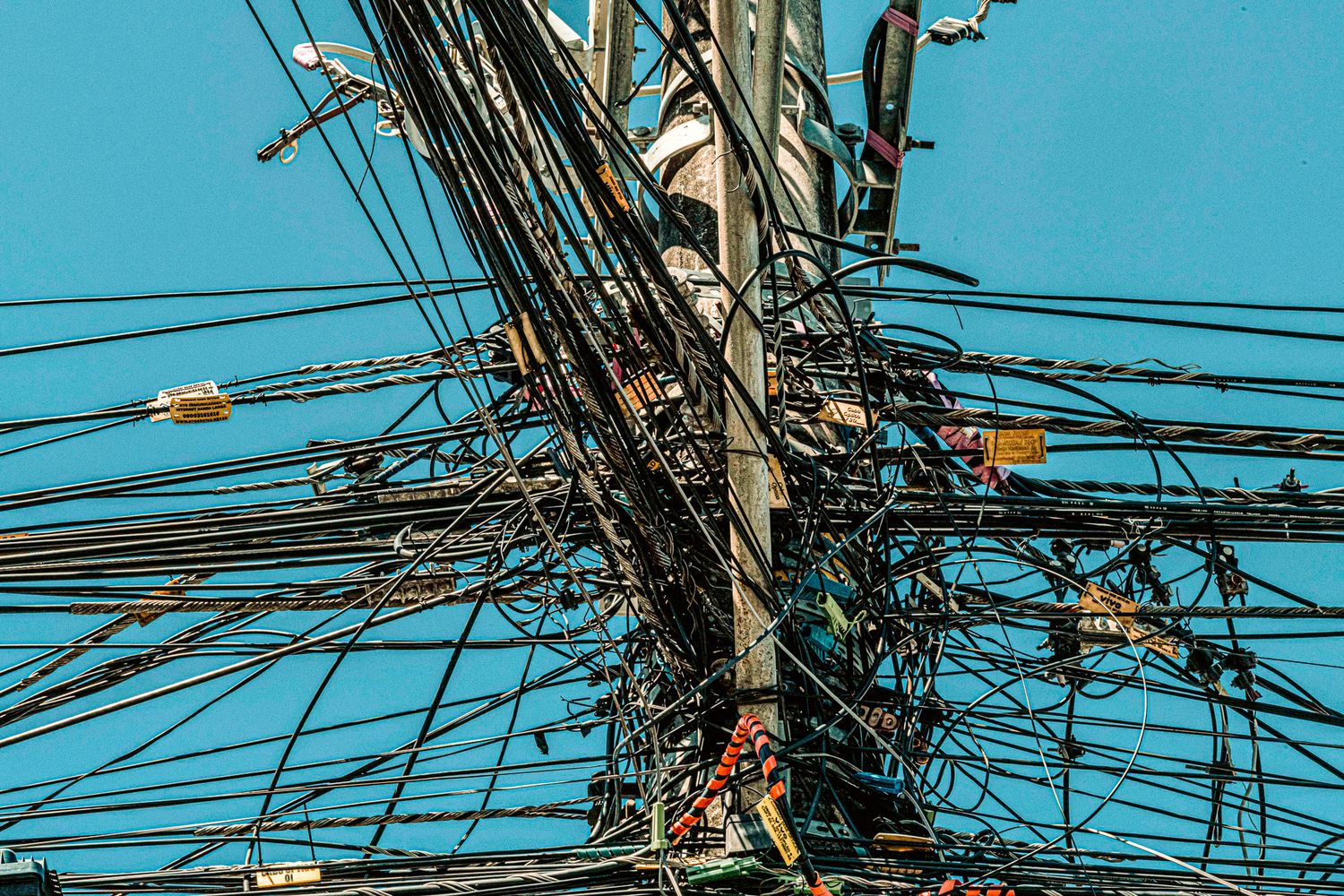 Chaotic tangle of electrical wires and cables on utility pole against blue sky.