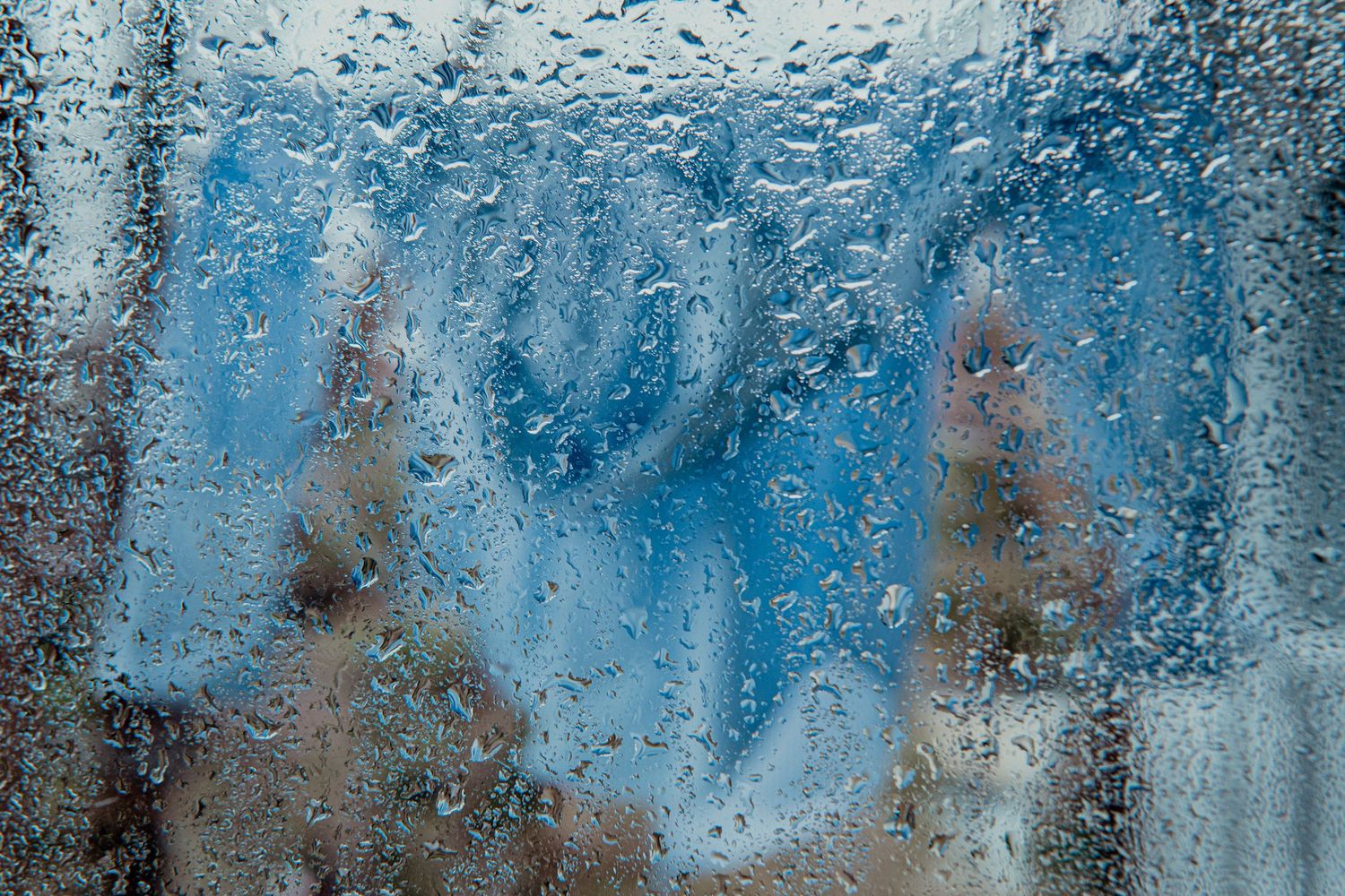 Water droplets on glass window with blue sky background creating abstract pattern.