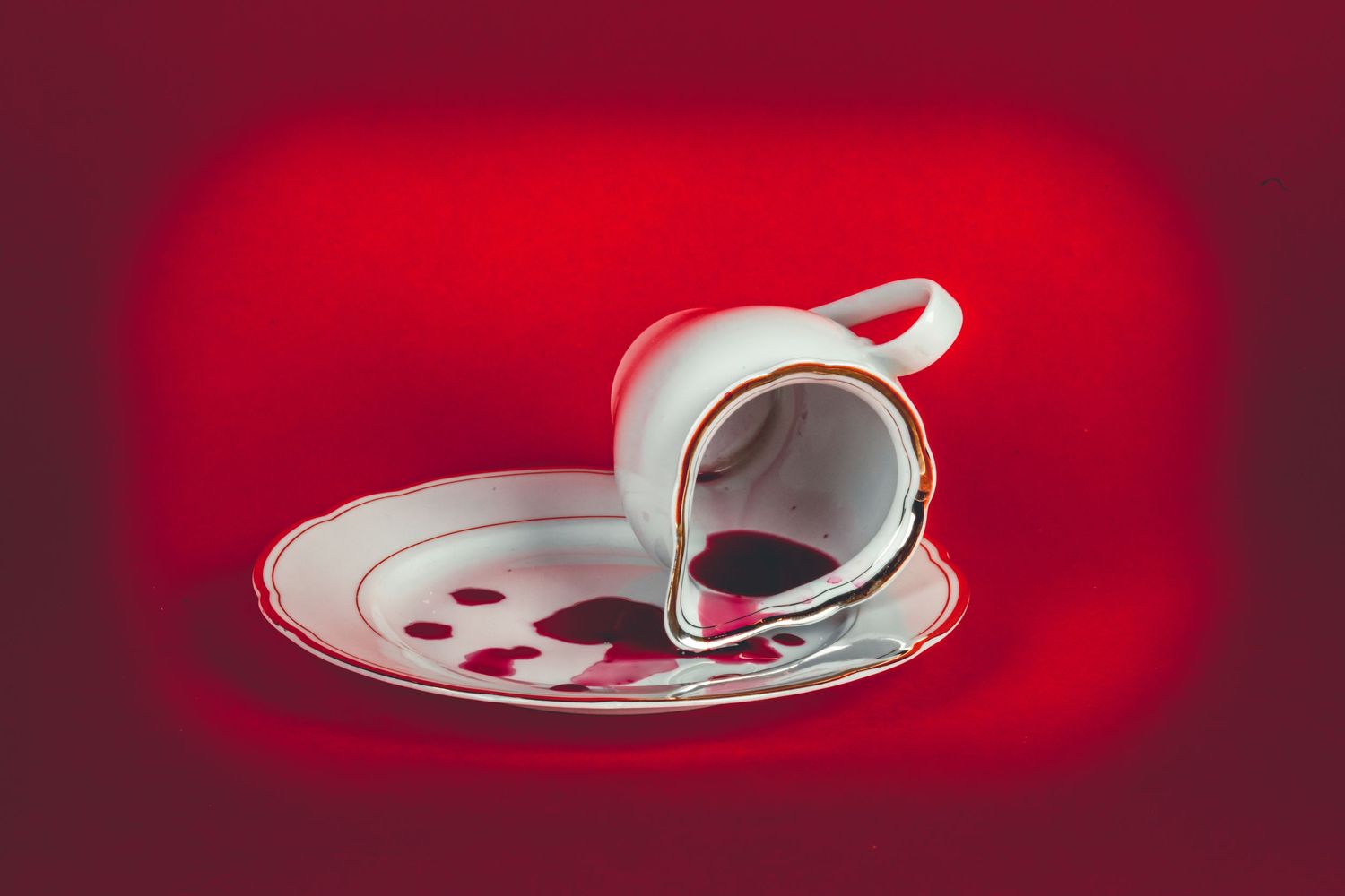 White teacup and saucer with dramatic lighting against deep red background.