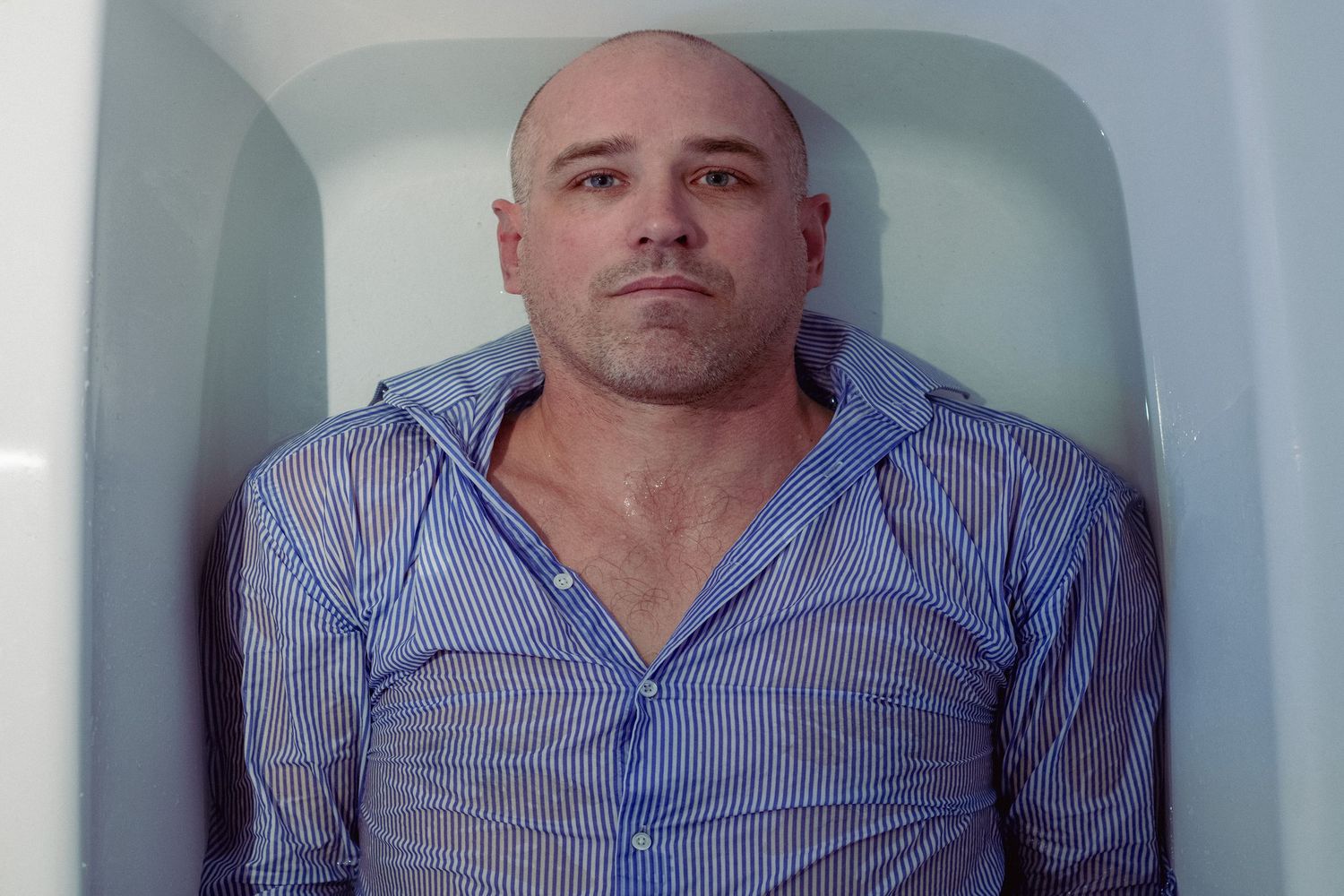 Person in striped shirt sitting against white wall.