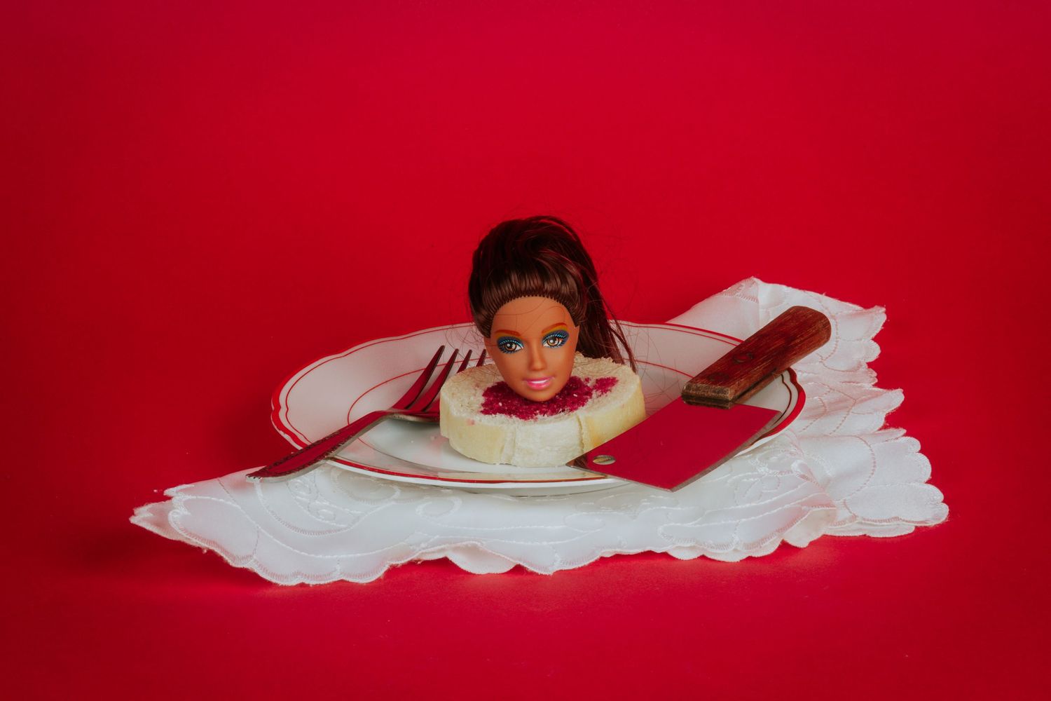 Figure draped in white fabric lying against red background in artistic composition.