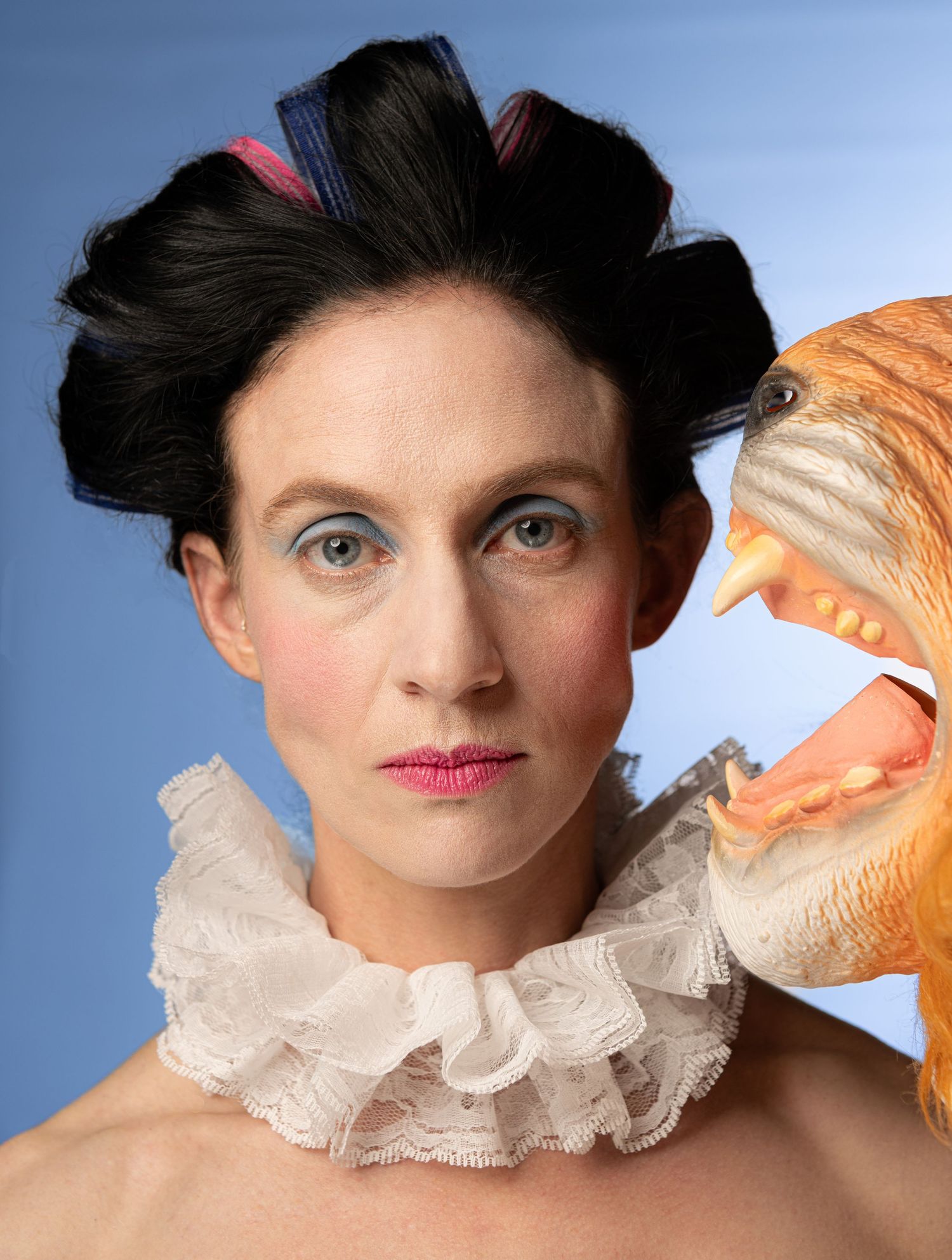 Artistic portrait with ruffled collar and orange prop against blue background.