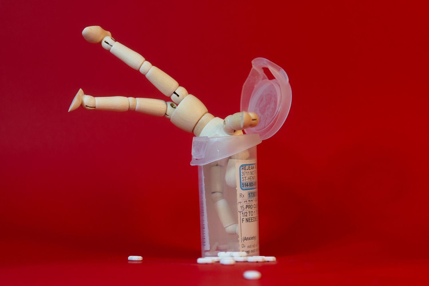 Wooden artist mannequin diving headfirst into medical syringe against red background.