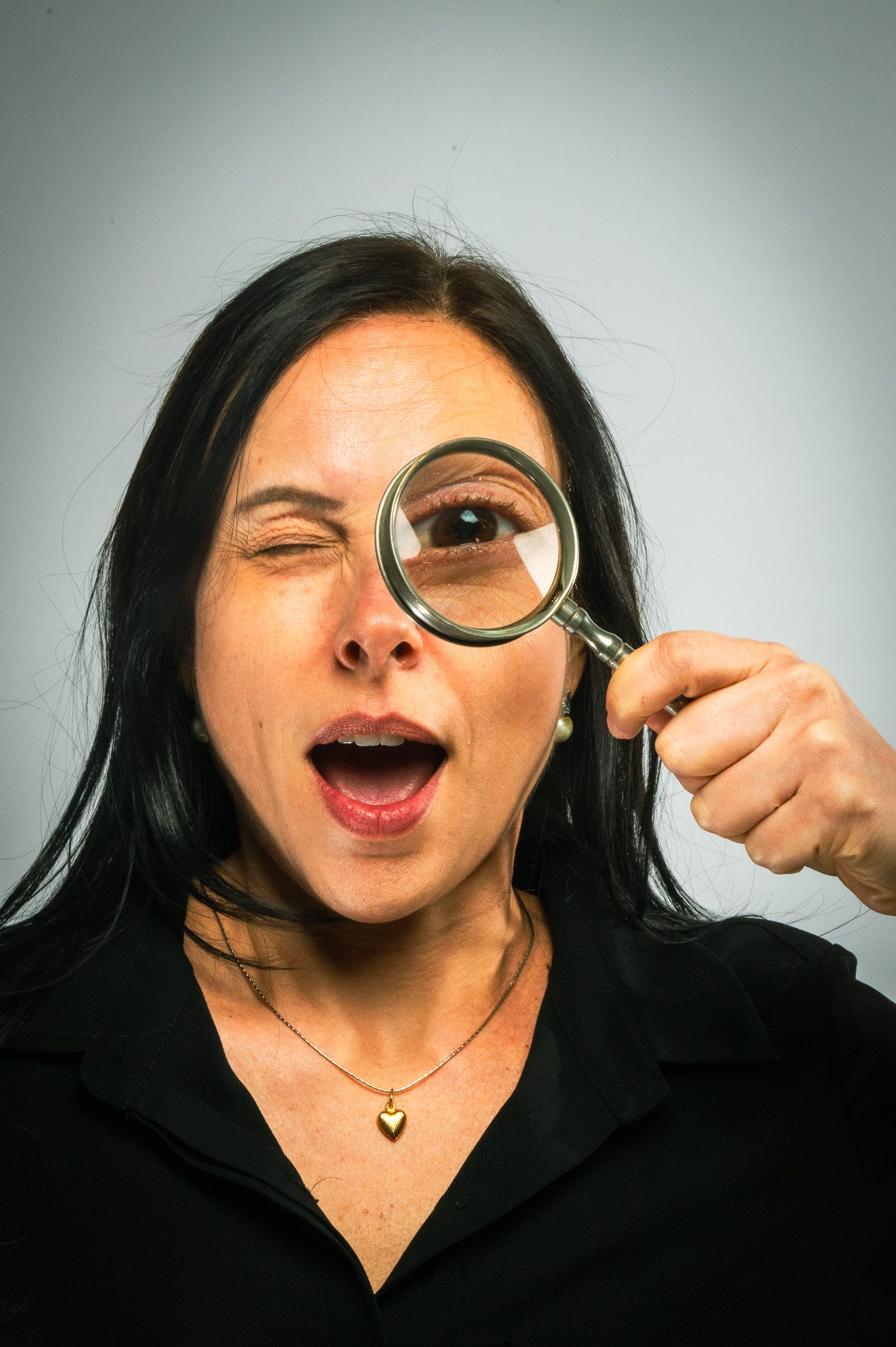 Playful portrait of woman looking through magnifying glass with surprised expression.