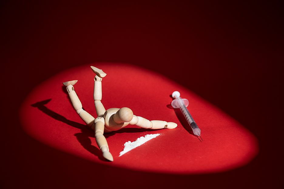 Wooden mannequin figure lying in dramatic red spotlight with pen nearby.