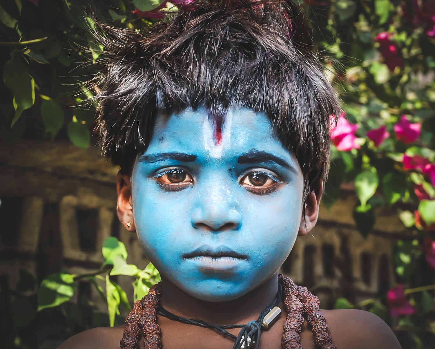 Close-up portrait with vibrant blue face paint and traditional tribal decorations.