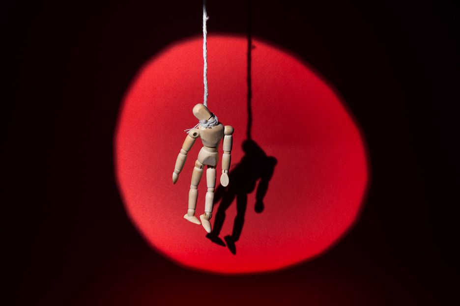 Wooden mannequin figure hanging from string against dramatic red circular backdrop.