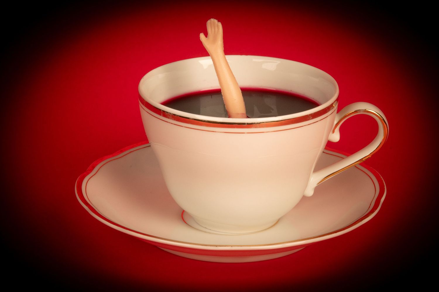 Teacup and saucer with wooden spoon photographed against dark red vignette background.
