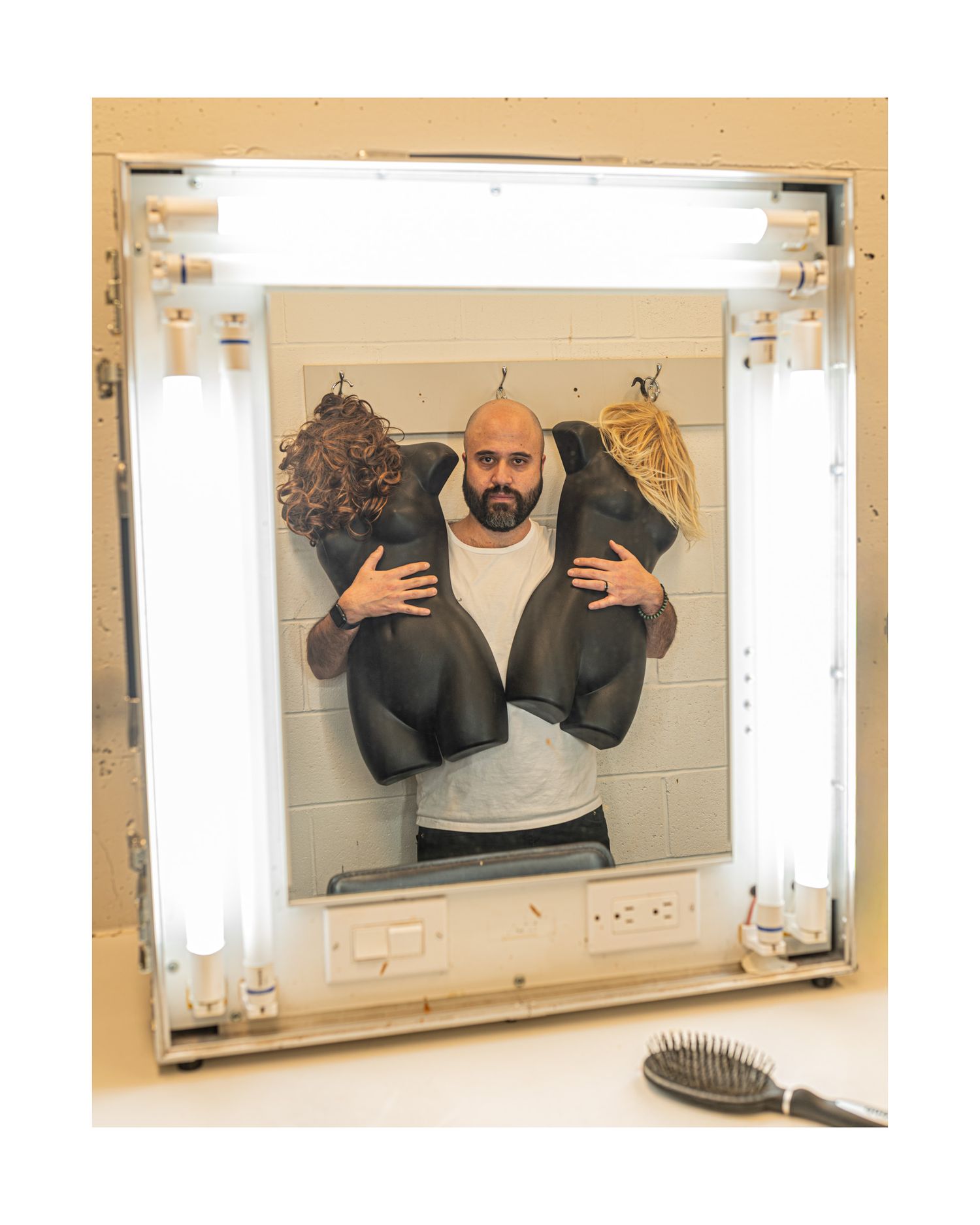 A bathroom mirror reflection shows someone gesturing with both hands in a dark shirt.