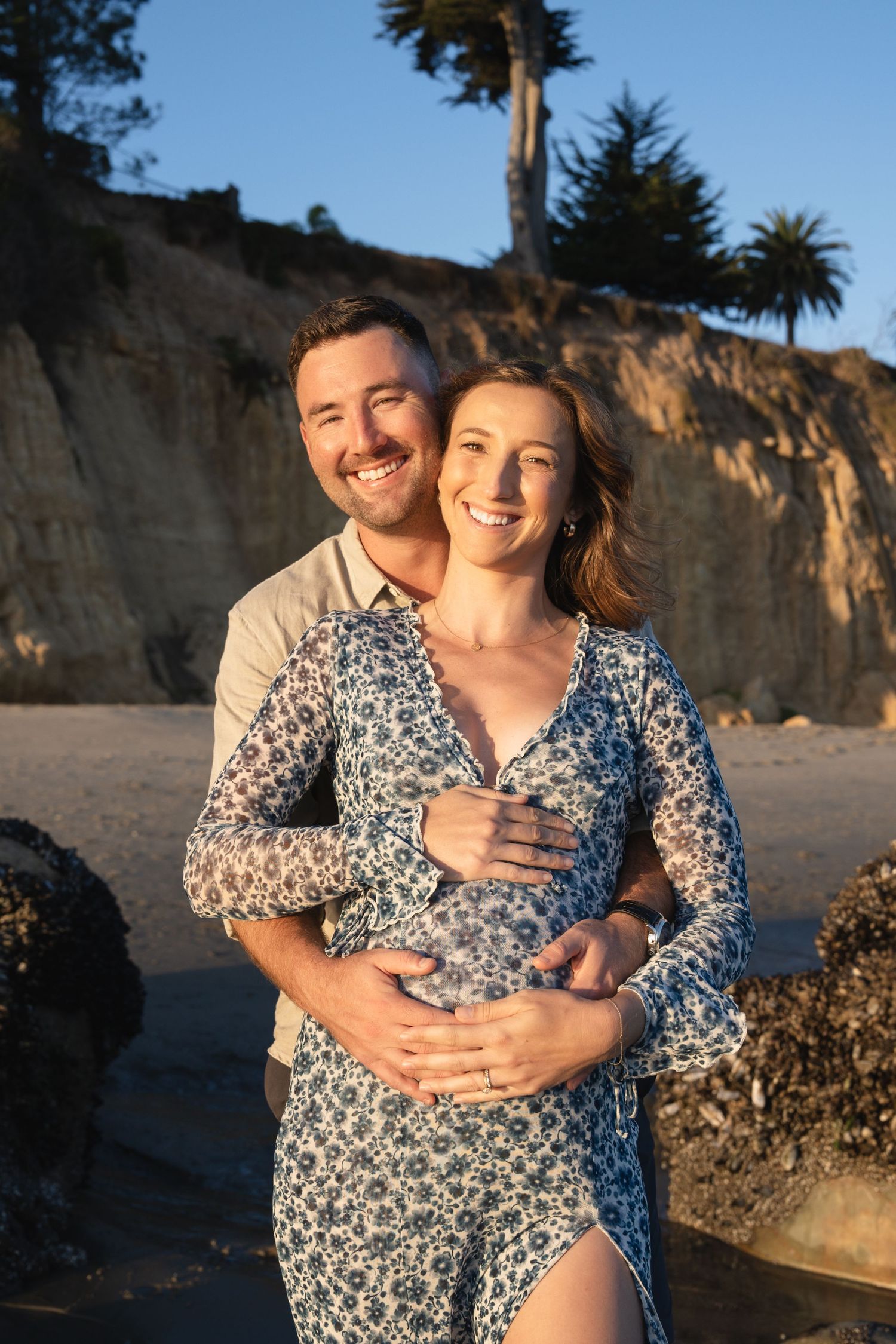 Romantic sunset beach photoshoot with couple embracing against coastal cliffs.