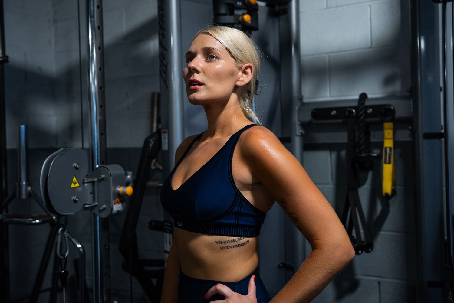 Athletic woman performing deadlifts with yellow weight plates in a dark industrial gym setting.