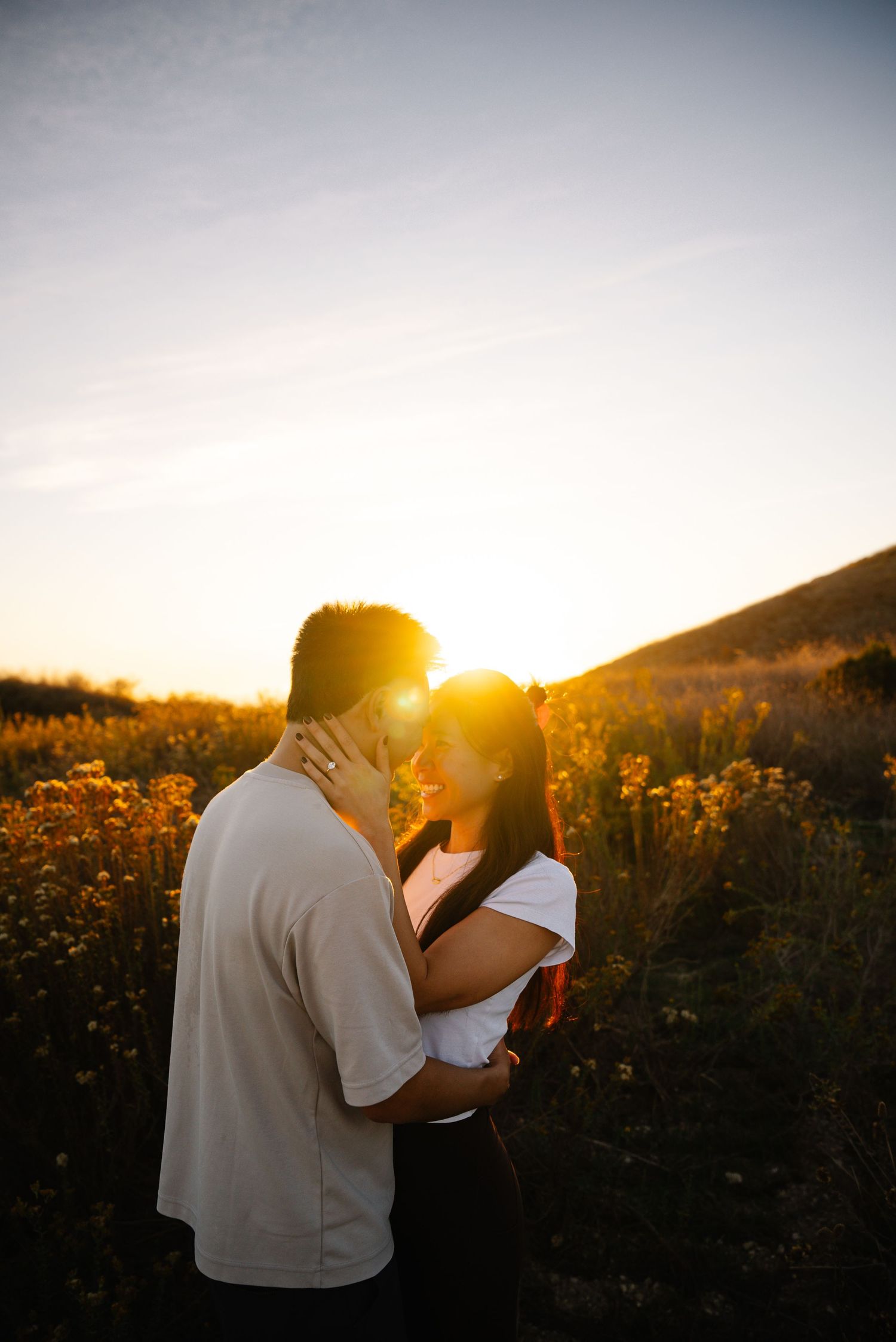 Intimate couple's silhouette against golden sunset in field of flowers.