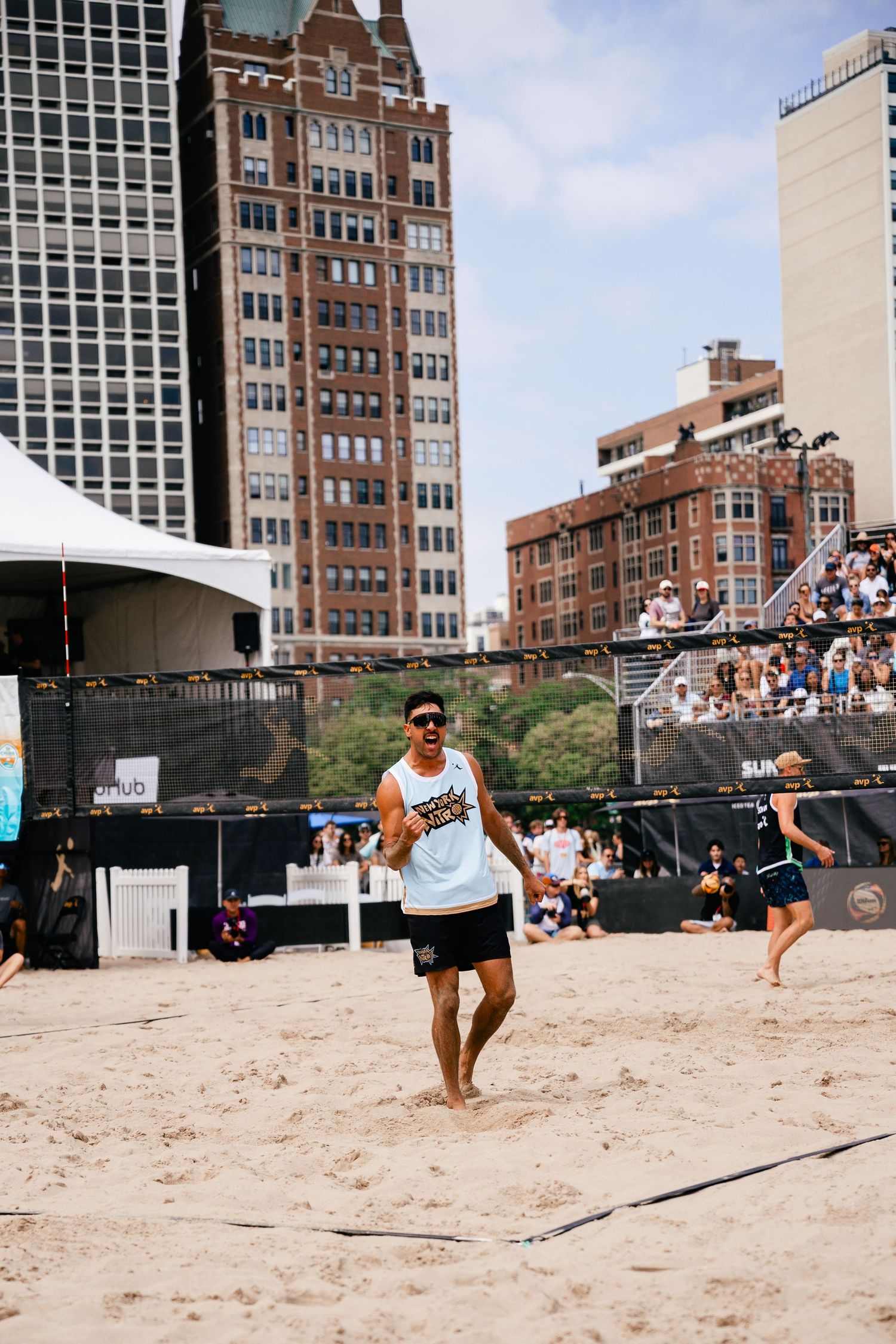 Athletes playing beach volleyball at urban tournament with buildings in background.