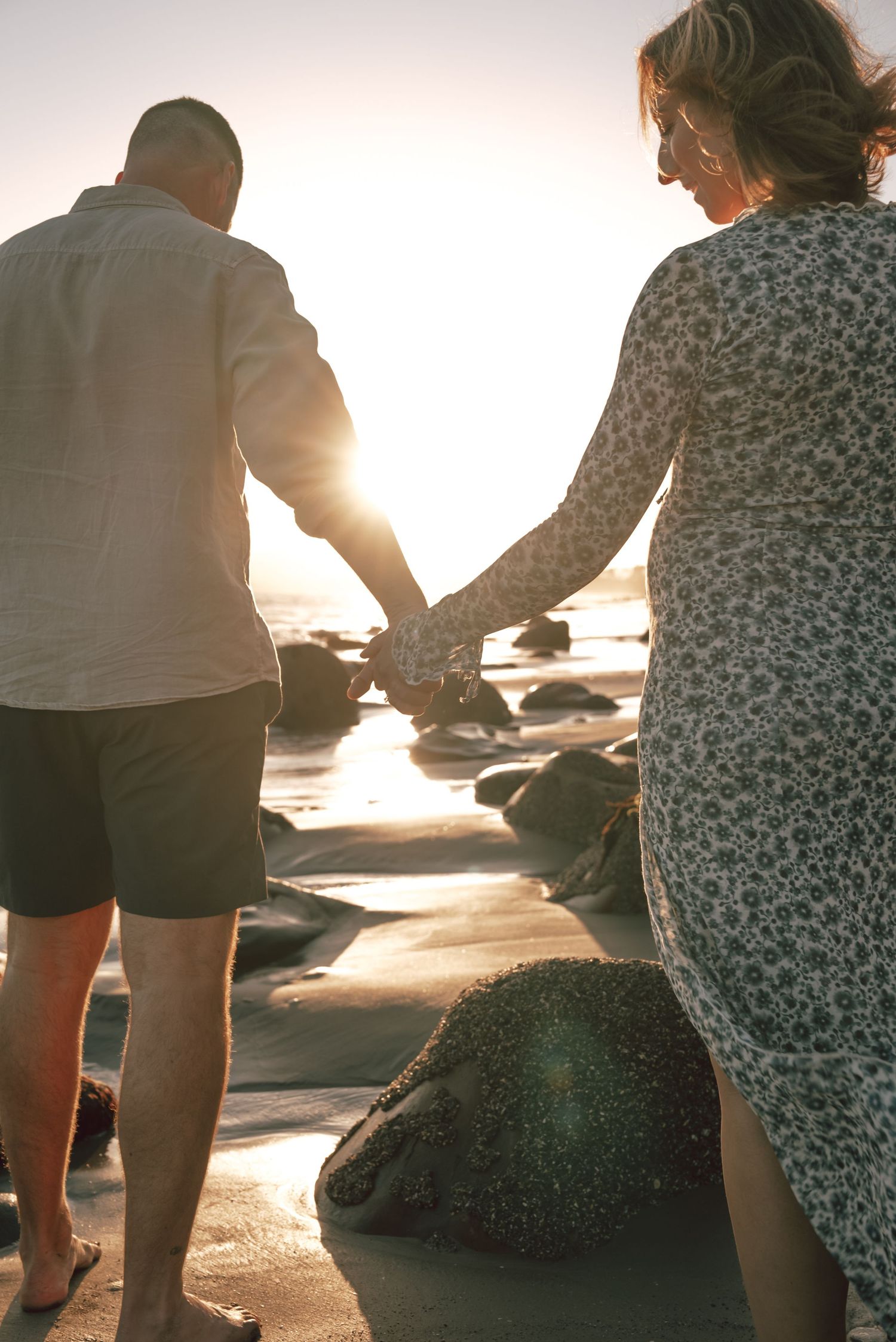 Couple sitting together on rocky beach during golden hour sunset.