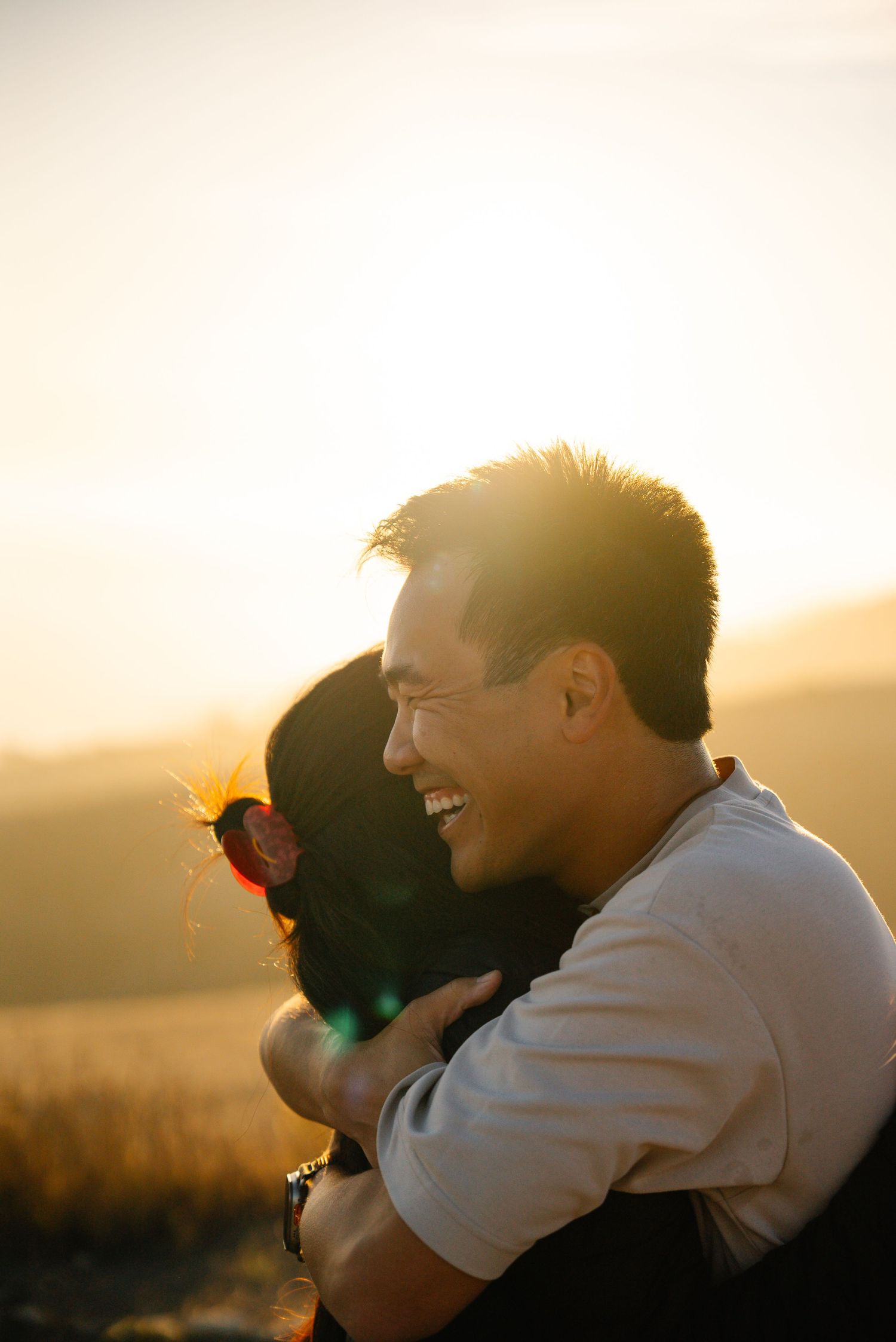Joyful couple embracing and laughing during sunset photo session.