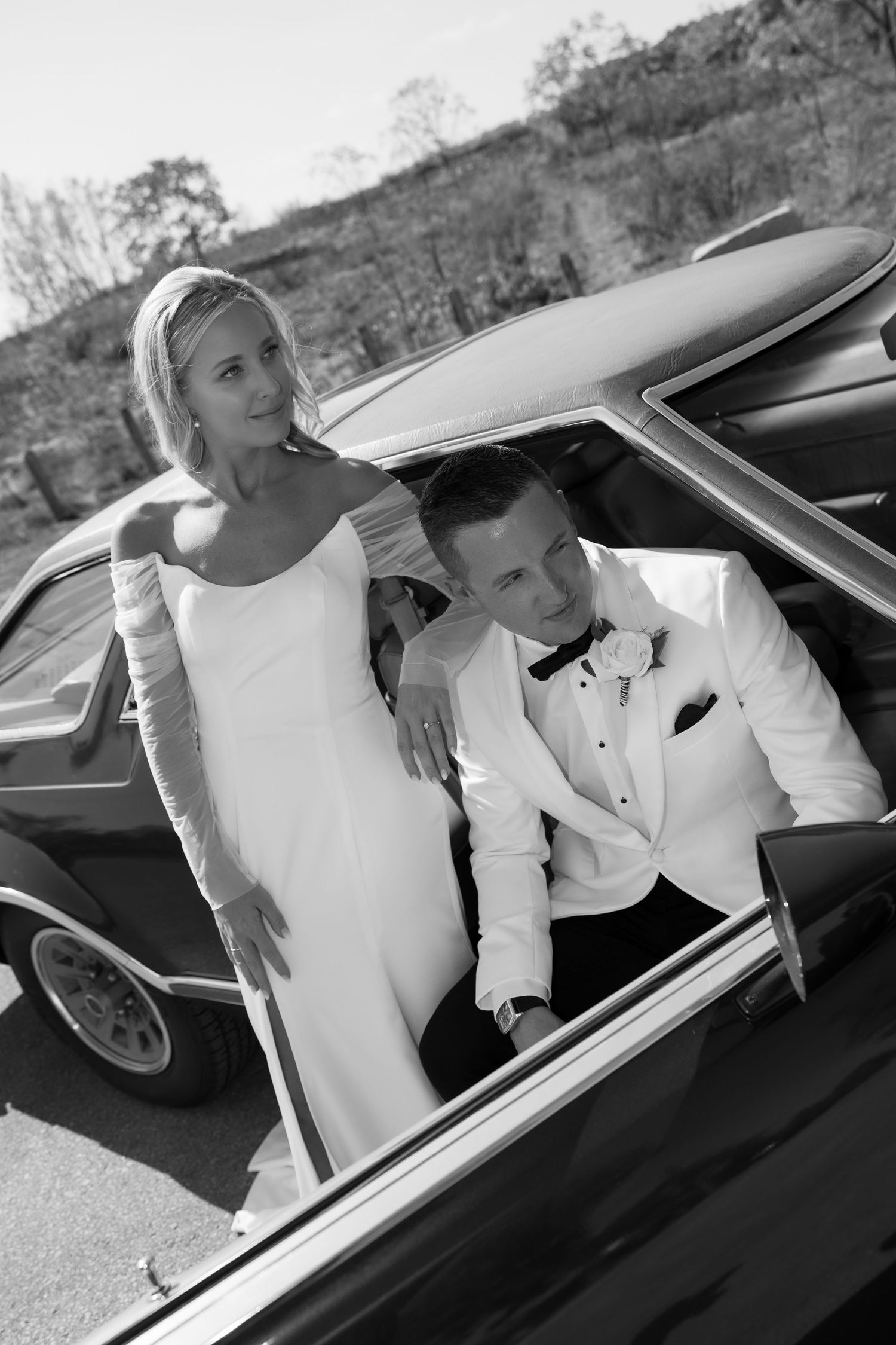 Wedding couple poses in a classic car with scenic mountain backdrop.