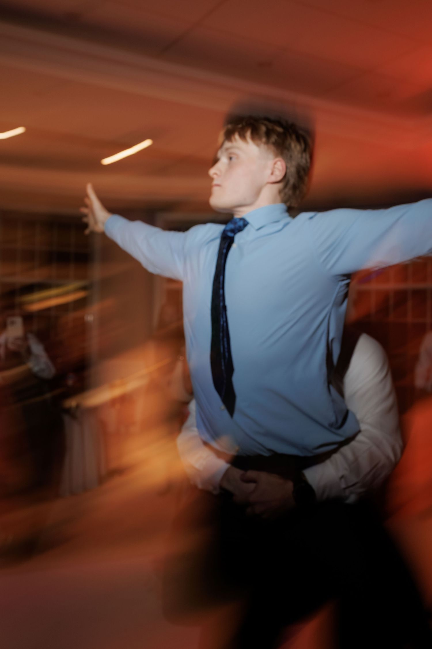 Guest in blue shirt dancing energetically at wedding reception with motion blur.