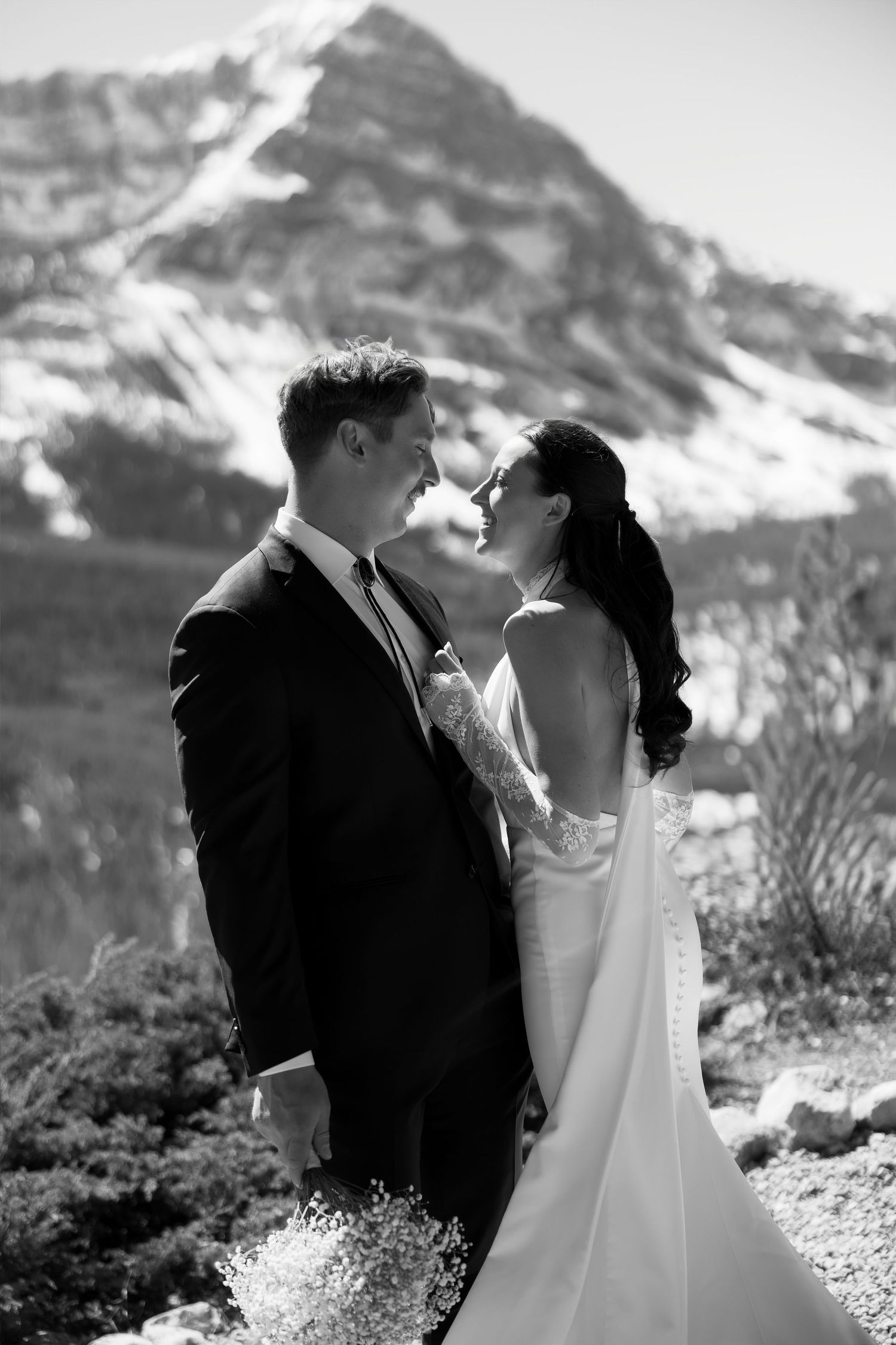 Black and white photo of bride and groom embracing with snow-capped mountain backdrop on their wedding day.