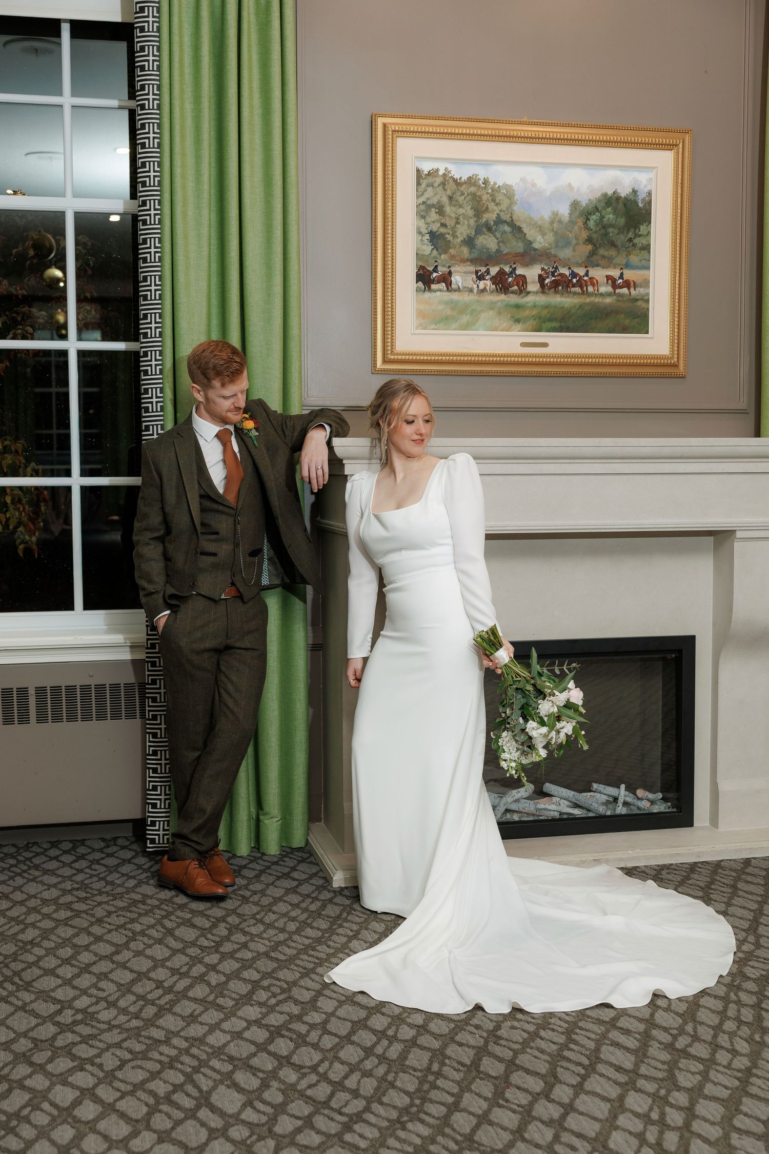 Wedding couple poses for romantic portraits in an elegant room with green curtains and a fireplace.
