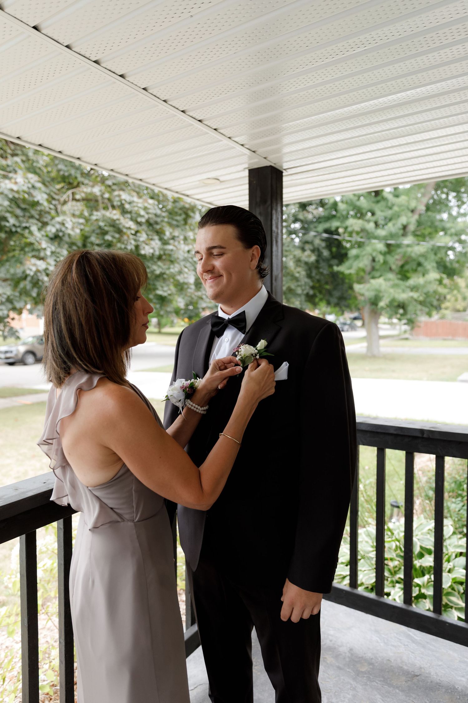 Wedding party helping with boutonniere preparation on covered porch.